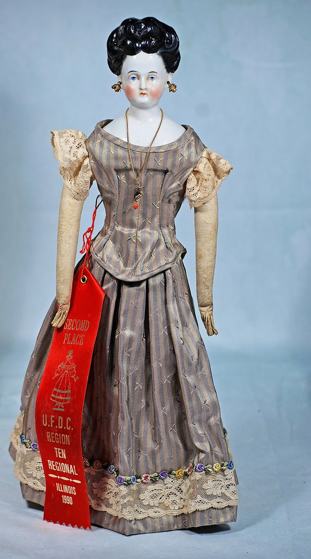 GERMAN PORCELAIN LADY WITH PIERCED EARS AND ORNATE COIFFURE: 16”. Porcelain shoulderhead, sculpted black hair waved away from face into an arrangement of elaborate curls with sculpted center ornament, stippling detail at the sides, ringlet curls at the ba