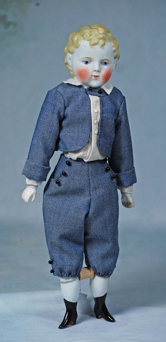 GERMAN PORCELAIN BOY WITH SCULPTED BLONDE HAIR: 15”. Porcelain shoulderhead with sculpted blonde curls, fully modeled ears, painted features, blue eyes, red and black eyeliner, tapered brows, closed mouth, cloth body with porcelain lower limb