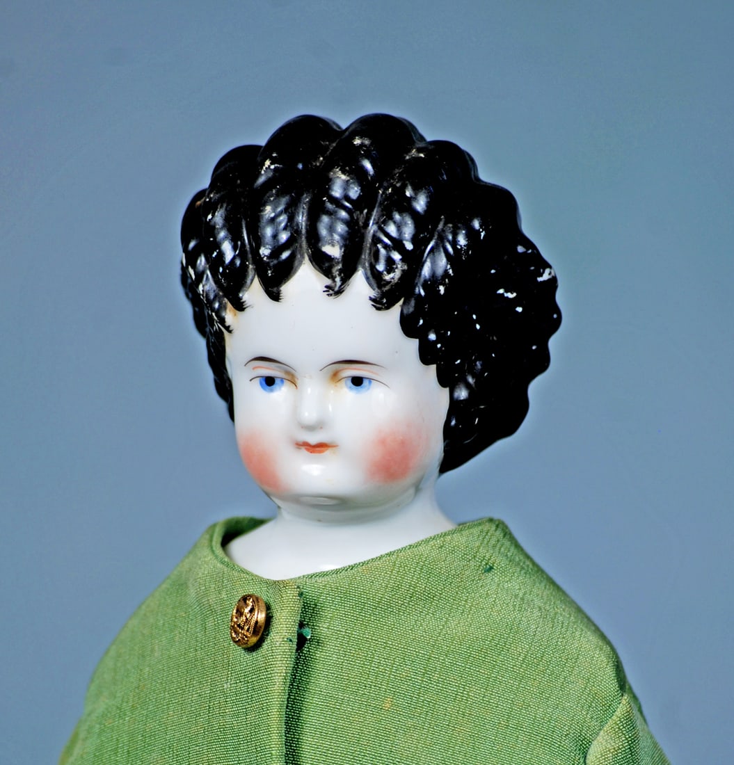 GERMAN PORCELAIN LADY WITH BLACK SPILL-CURL COIFFURE: 15”. Porcelain shoulderhead, sculpted black hair arranged in finger curls that “spill” onto her forehead, painted blue eyes, upper eyeliner, tapered brows, closed mouth, old muslin b