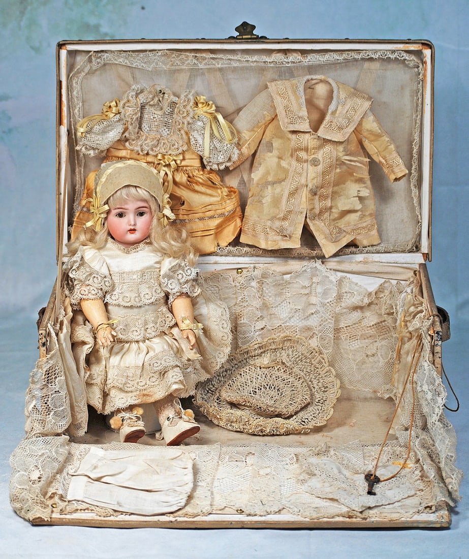GERMAN BISQUE CHILD BY KAMMER AND REINHARDT IN PRESENTATION TRUNK: Trunk 13 ½” W x 8” H.; doll 11”. Marks: K * R Germany. Bisque socket head, brown sleep eyes, painted lashes, feathered brows, pierced ears, open mouth, accented lips, upper teet
