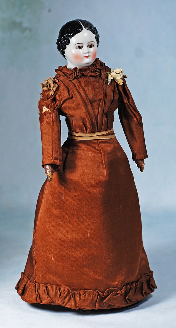 GERMAN PORCELAIN LADY WITH BROWN GLASS EYES: 15”. Porcelain shoulderhead, sculpted black hair, center-parted with comb-mark details and tiny curls all around, inset large brown glass eyes, painted lashes, black and red eyeliner, tapered br