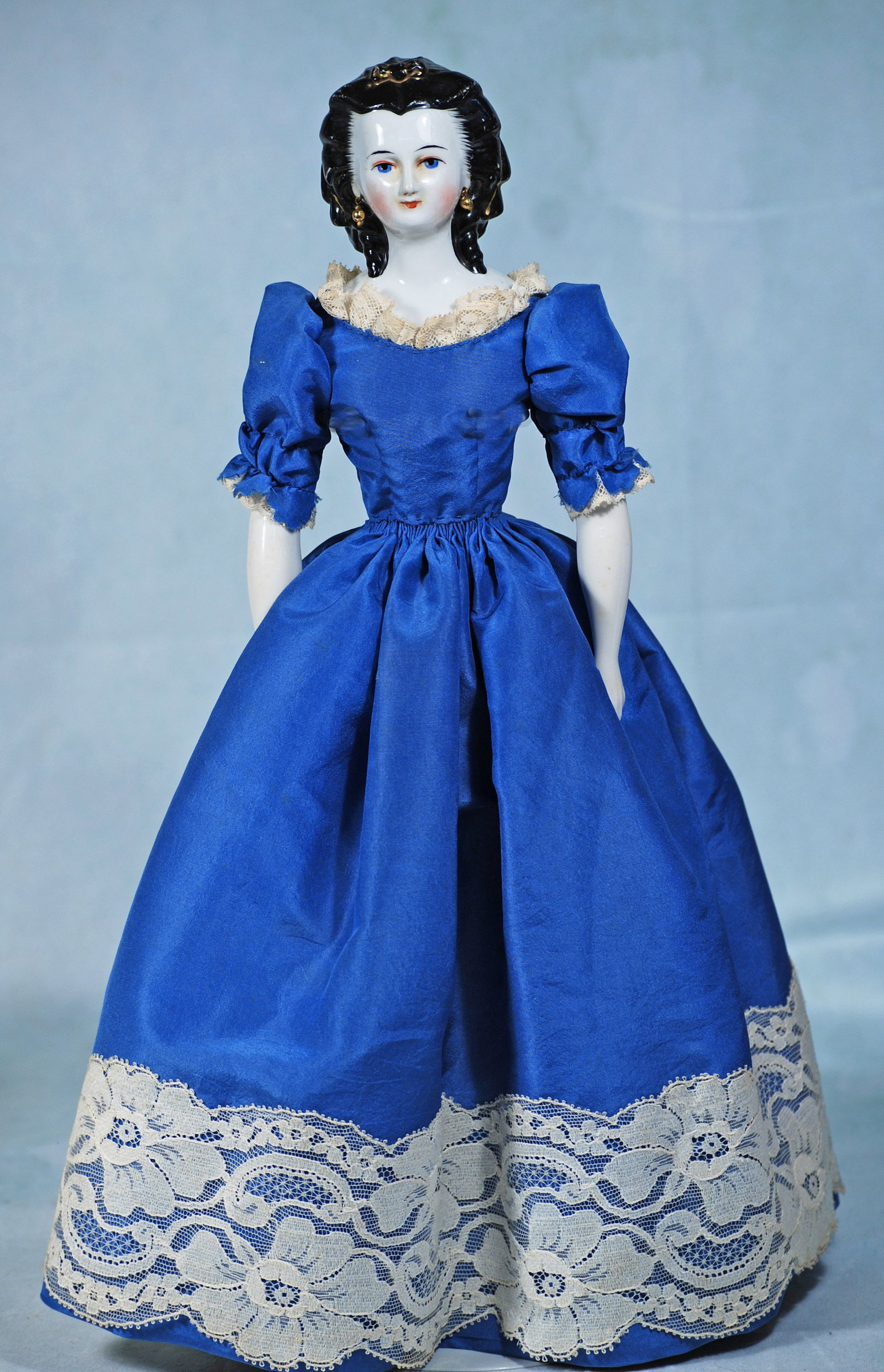 GERMAN PORCELAIN YOUNG LADY WITH GILT SNOOD AND ELABORATE COIFFURE: 16”. Porcelain shoulderhead with black sculpted hair with distinct widows peak, hair drawn away from face and formed into rolled curls at the sides with stippling detail, ringlet curls falling
