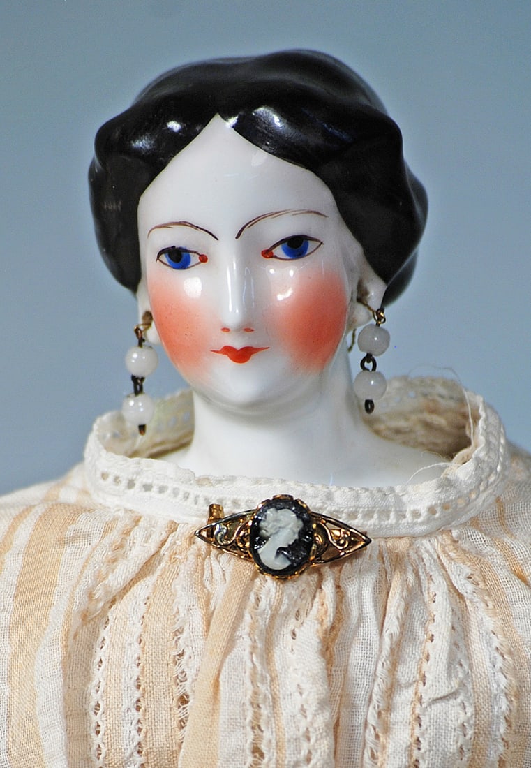 FRENCH PORCELAIN LADY WITH OUTLINED BLUE EYES: 14”. Porcelain shoulderhead with painted cobalt blue eyes outlined all around, lightly feathered brown brows, closed mouth, pierced ears, sculpted black hair waved away from the face into a