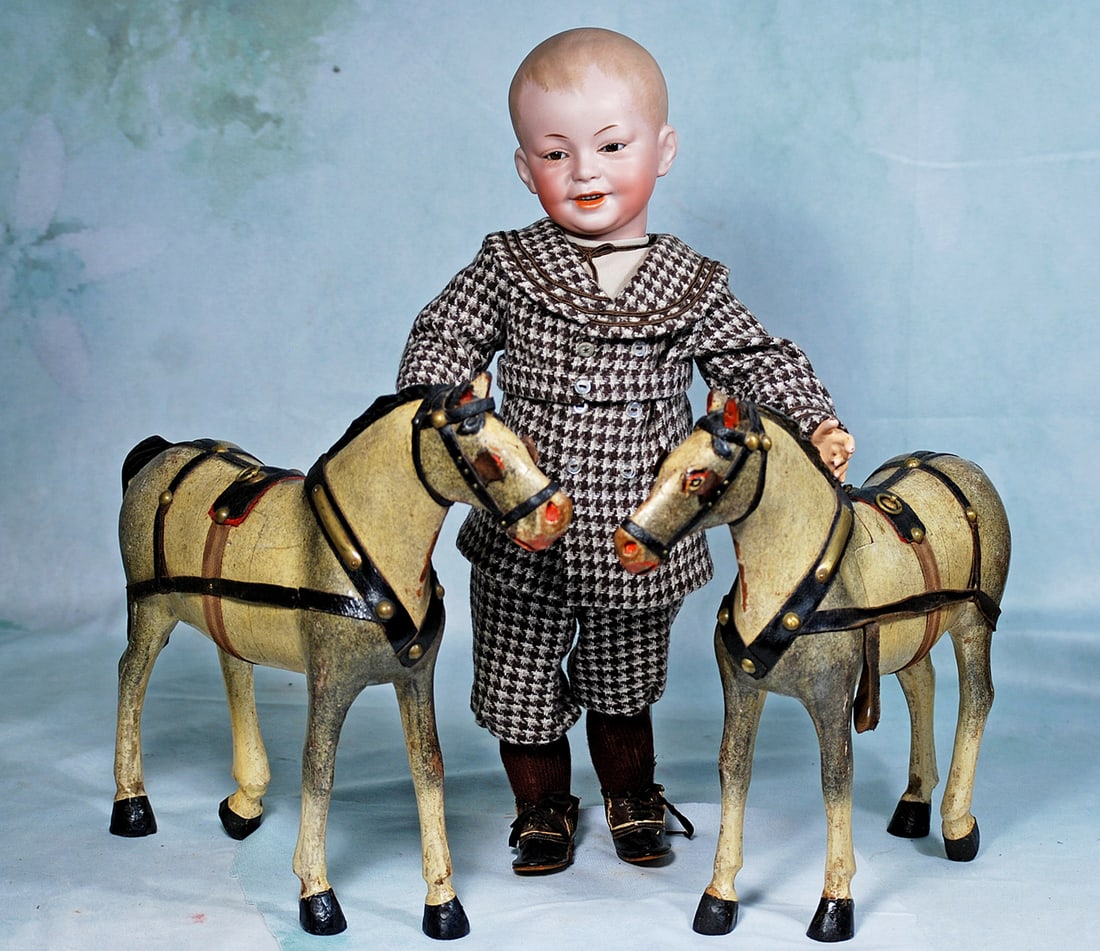 PAIR OF GERMAN CARVED WOODEN TOY HORSES: 12”. Each is carved wooden horse with well-defined dappled finish, carved mane with deep comb marks, stippled feathering, carved tail, leather harness with brass studs, leather blinders.