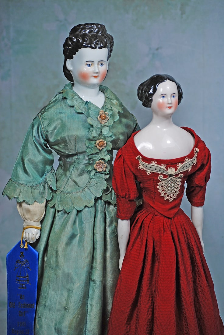 GERMAN PORCELAIN LADY WITH PINK-TINTED COMPLEXION: 18”. Porcelain shoulderhead with pink-tinted complexion, black sculpted hair is center parted, side braids pulled to the back of the head into a braided two-strand coil, painted features, blue e