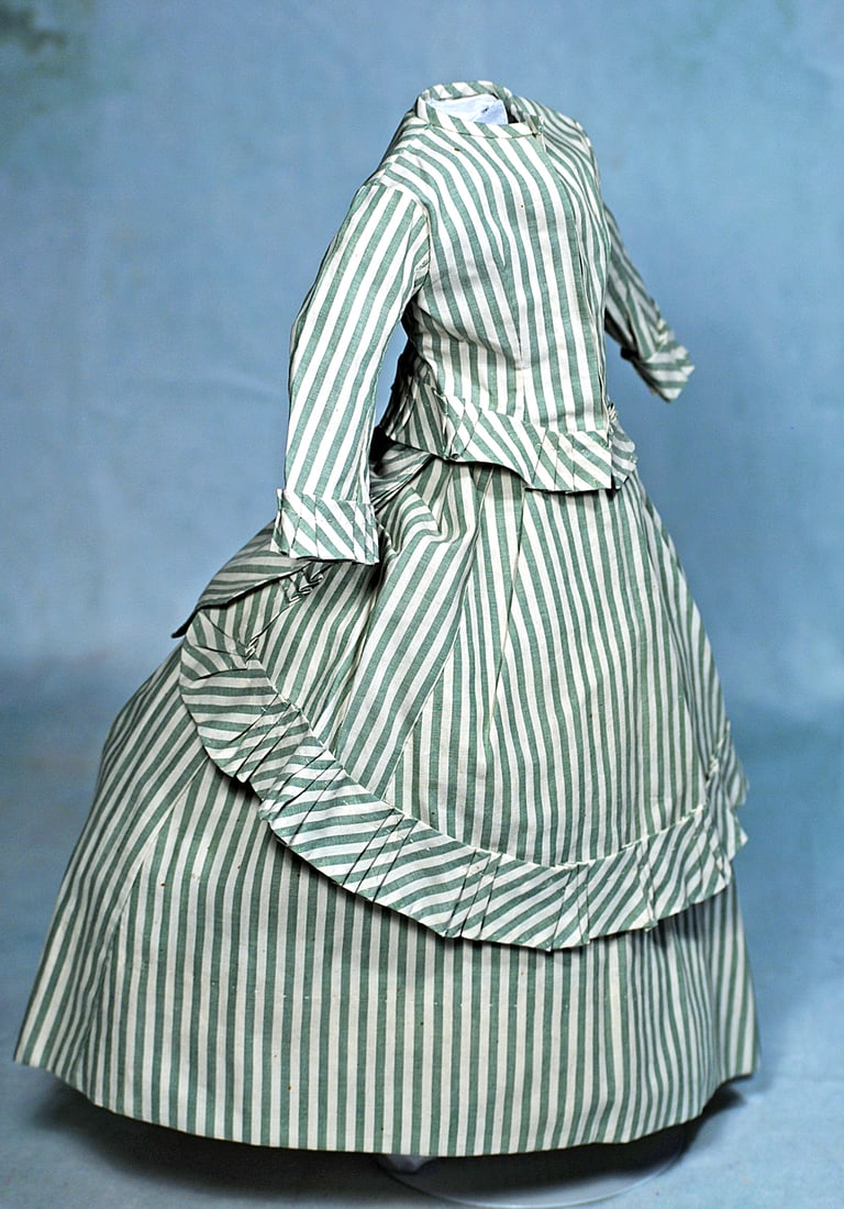 GOWN FOR FRENCH POUPEE BY SYLVIA MAC NEIL: Two-piece gown of green and cream striped cotton features a dart-shaped front and back, drawn up at the sides and garnished at center back with layered bow, gathered ruffle all around and forming a bu