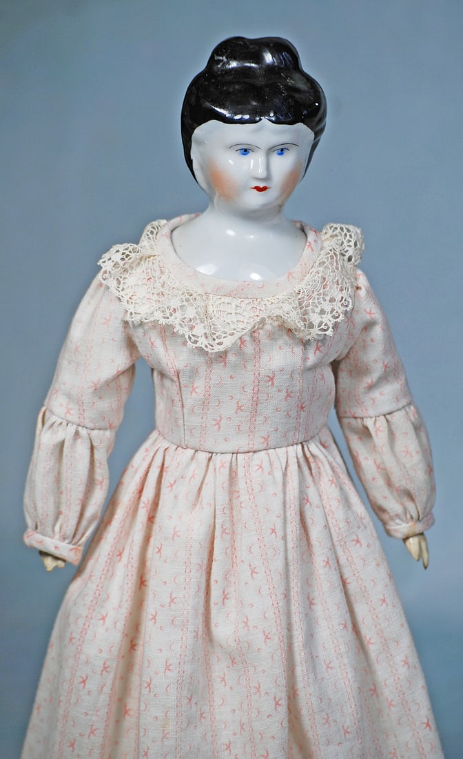 GERMAN PORCELAIN LADY: 13 ½”. Porcelain shoulderhead with sculpted black hair waved away from face and pulled high on the head into an arrangement of layered curls, painted features, blue eyes, red and black eyel