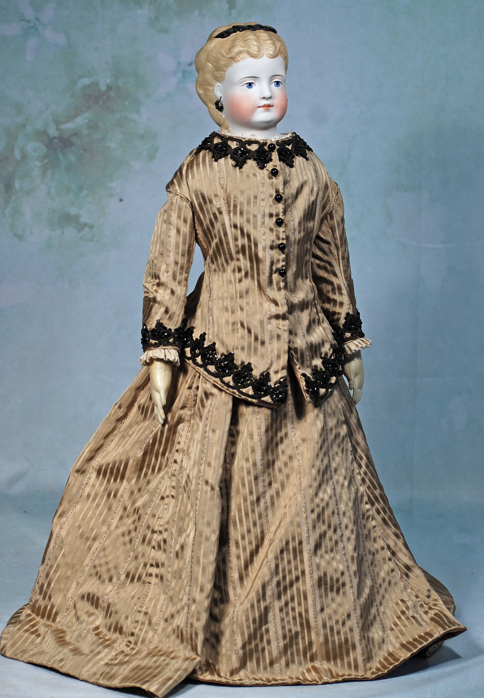 GERMAN BISQUE LADY WITH SCULPTED HAIR AND PIERCED EARS: 22”. Marks: None visible. Bisque shoulderhead with sculpted blonde hair waved away from her face and secured with a sculpted black headband, modeled and pierced ears, clusters of ringlet curls i