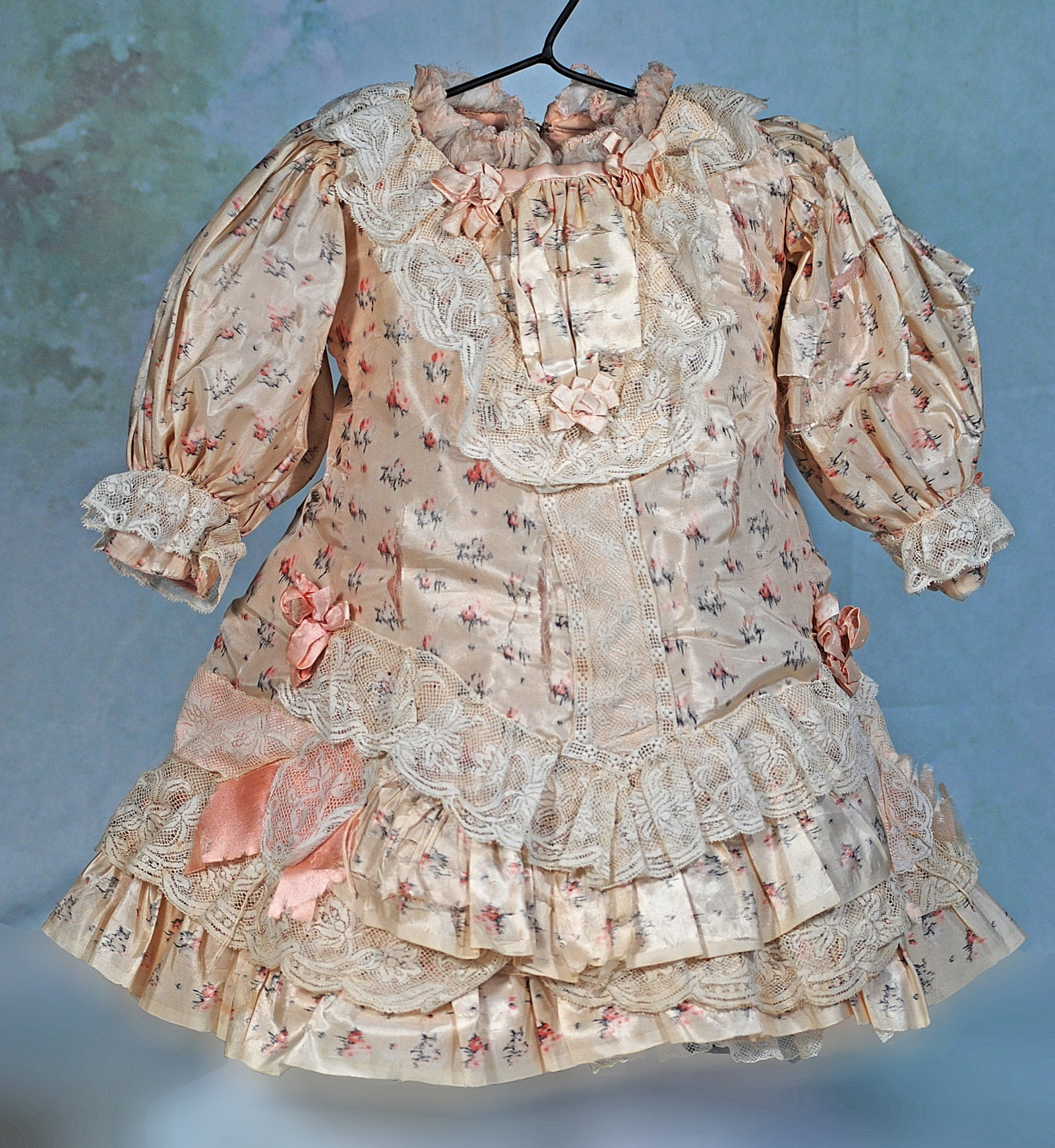 FANCY SILK DOLL DRESS: 7 ½” shoulder width; 18” length. Pale pink silk rosebud print made up in a French-style dress with princess styling, tiers of ruffles with scalloped lace trim, puffed sleeves, tiny