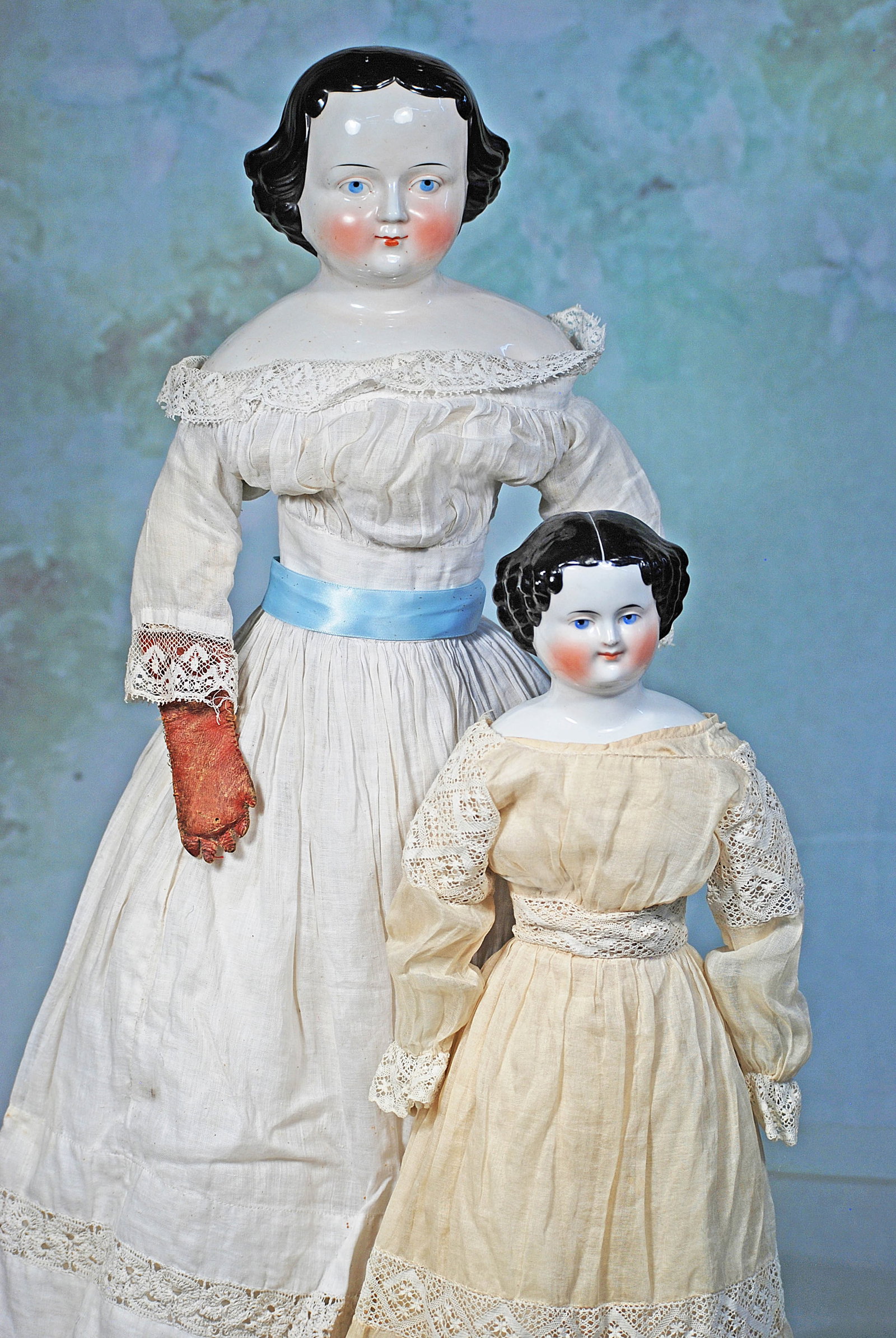 TWO GERMAN PORCELAIN LADY DOLLS.: 274. TWO GERMAN PORCELAIN LADY DOLLS. 29” and 21”. Each is porcelain shoulderhead with sculpted short black hair arranged in wave and curls, painted features, blue eyes, red and black
