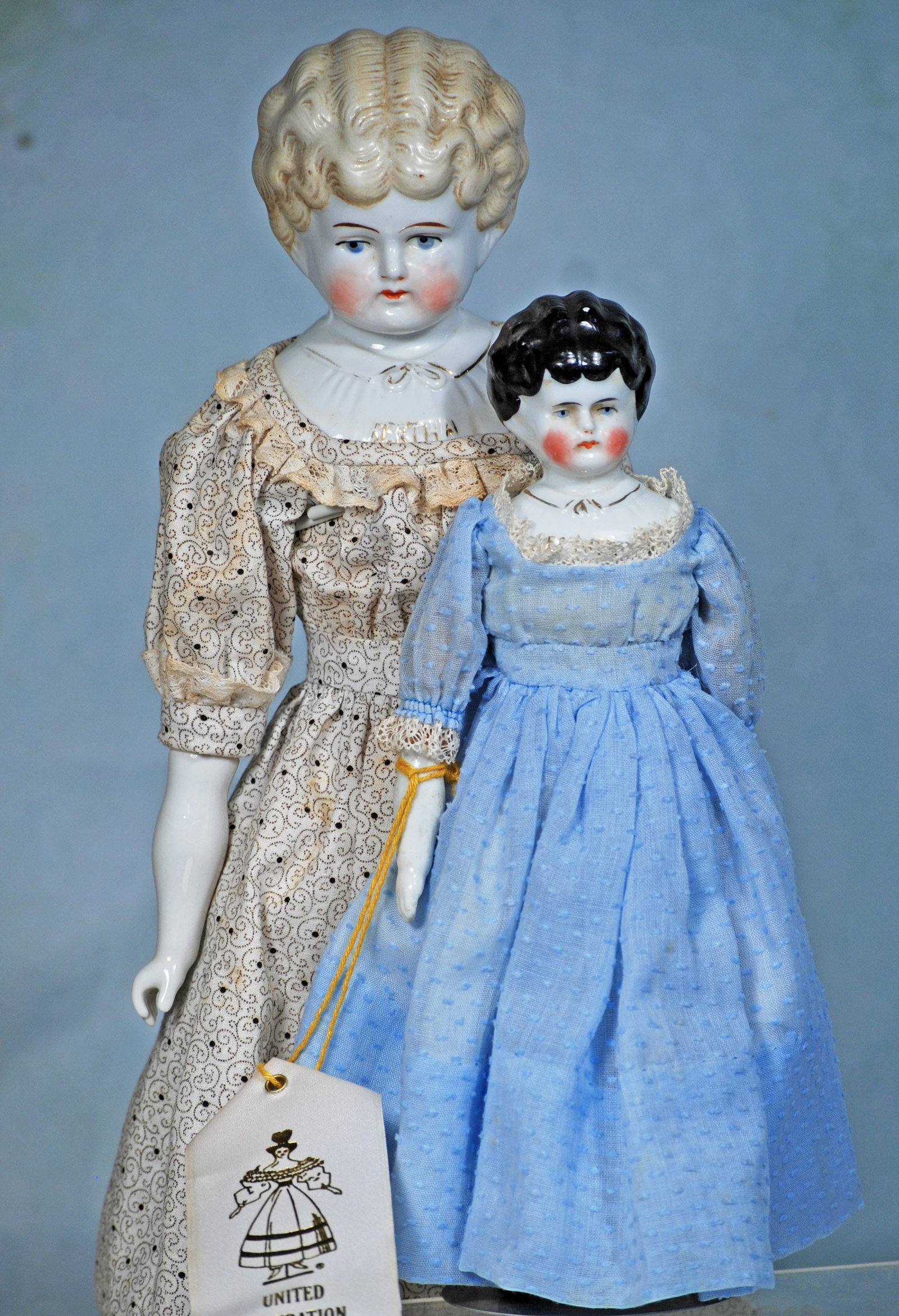 TWO PET NAME PORCELAIN LADY DOLLS: 275. TWO PET NAME PORCELAIN LADY DOLLS. 10” and 17”. Each is porcelain shoulderhead with sculpted short hair arranged in all-over curls, painted features, blue eyes, tapered brows, closed