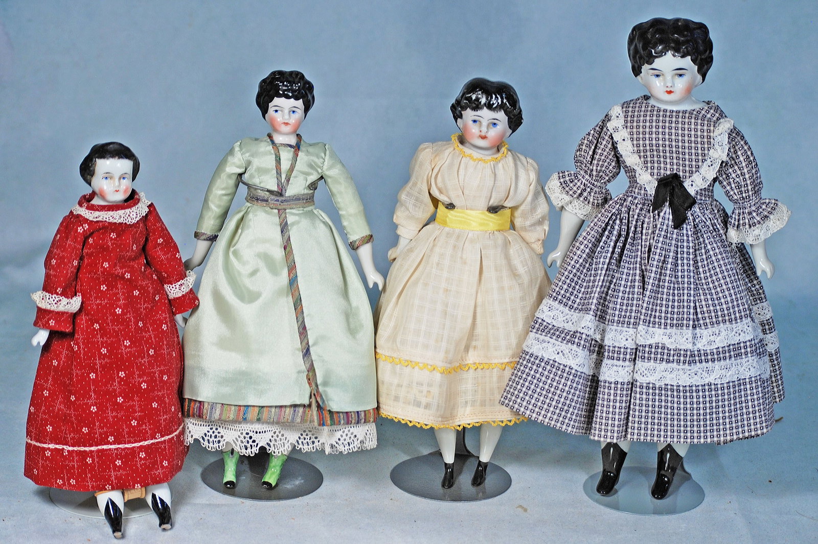 FOUR SMALL GERMAN PORCELAIN LADY DOLLS: 292. FOUR SMALL GERMAN PORCELAIN LADY DOLLS. 9 ½” to 12”. Each is porcelain shoulderhead with sculpted black curly hair, painted features, blue eyes, closed mouth, cloth body, cotto