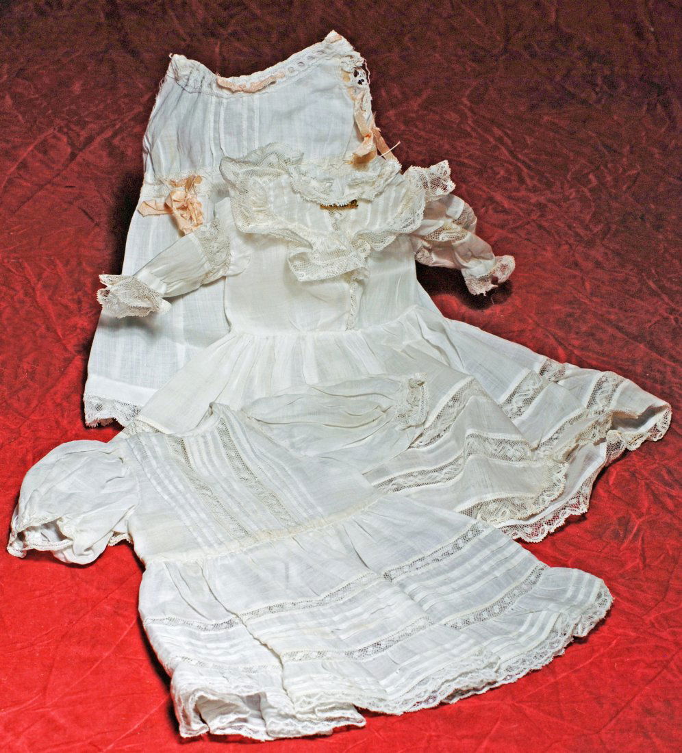 TWO ANTIQUE WHITE DOLL DRESSES. (1) White lawn dress: TWO ANTIQUE WHITE DOLL DRESSES. (1) White lawn dress has rounded yoke with tucks and lace ruffle, puffed sleeves and gathered skirt with insert lace and lace edging, gilt pin, 3 ¼” shoulder width,