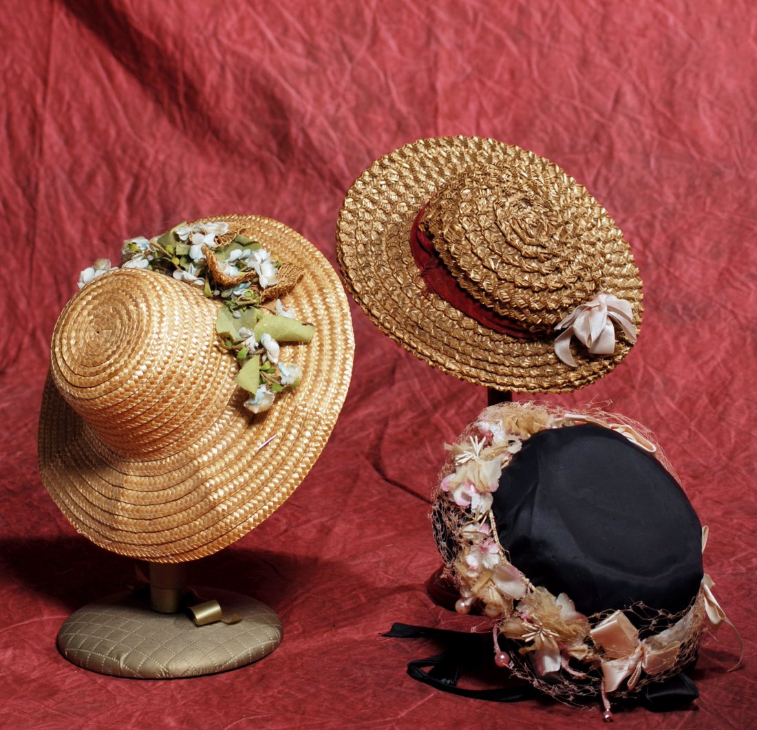 THREE DOLL BONNETS. (1) Woven natural color straw: THREE DOLL BONNETS. (1) Woven natural color straw bonnet with high crown, 2 ¾” brim with floral decorations, 4 ¼” inside cap width; (2) Intricately woven brown straw bonnet with 2 ½” graduate