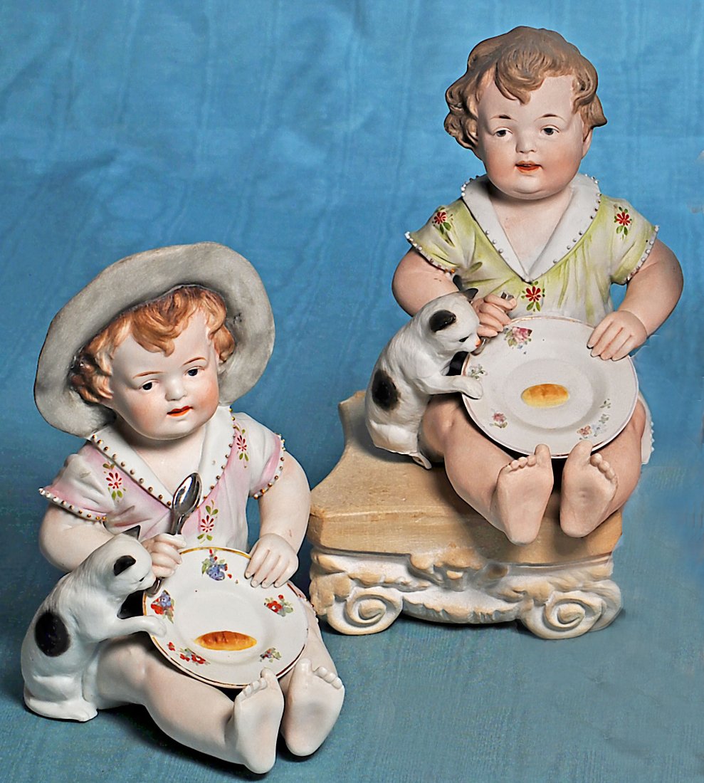 TWO GERMAN BISQUE PIANO BABIES WITH KITTENS. 8”. Each: TWO GERMAN BISQUE PIANO BABIES WITH KITTENS. 8”. Each is all-bisque seated baby with sculpted brown hair, painted features, brown intaglio eyes, tapered and shaded brows, open/closed mouth with mode