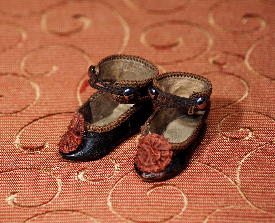 PAIR OF TINY FRENCH LEATHER DOLL SHOES: PAIR OF TINY FRENCH LEATHER DOLL SHOES. Length 1 ½”. Dark leather shoes with overcast edges, brown silk rosettes, ankle-strap closing. Commentary: Antique shoes in very good condition. Estimate: $1