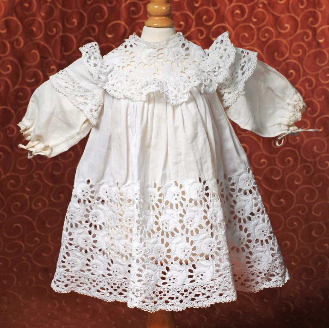 ANTIQUE WHITE DOLL DRESS: ANTIQUE WHITE DOLL DRESS. Fine white cotton dress with extensive cut-work detail, yoke with ruffled edge, gathered skirt, inset sleeves, back button closing; 4 ½” shoulder width, 11” length. Comm