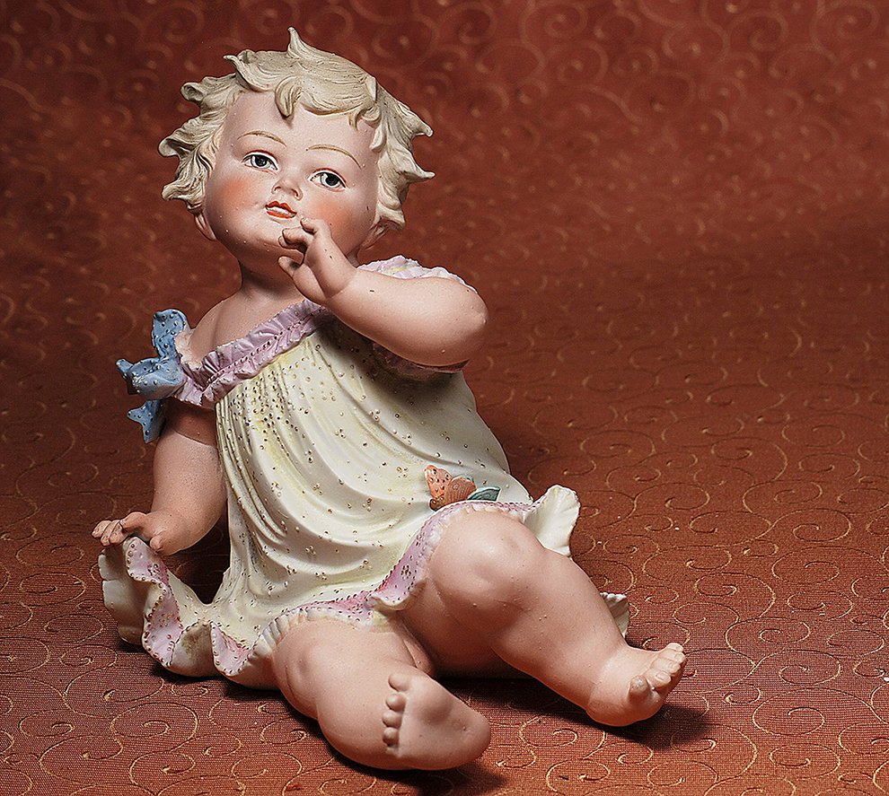 CONTA & BOEHME BISQUE PIANO BABY WITH BUTTERFLY: CONTA & BOEHME BISQUE PIANO BABY WITH BUTTERFLY. Marks: None. 9 ½”. Seated bisque child has sculpted wavy blonde hair, painted features, blue eyes with deep eyelids and eyeliner, shaded brows, open