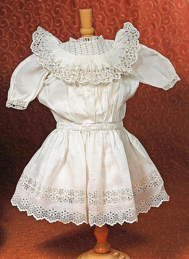 ANTIQUE WHITE COTTON DOLL DRESS: ANTIQUE WHITE COTTON DOLL DRESS. 6” shoulder width, 13” length. Fine white cotton dress has inset embroidered eyelet yoke with deep scalloped-edge eyelet ruffle, gathered bodice, three-quarter puf