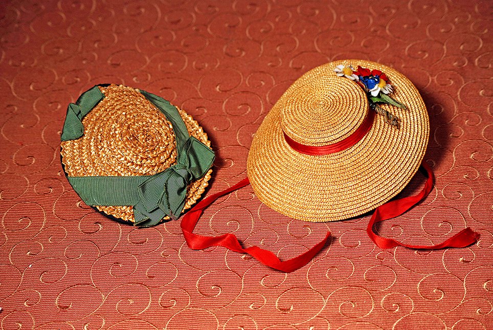 TWO STRAW DOLL BONNETS: TWO STRAW DOLL BONNETS. (1) Woven natural straw skimmer with green silk faille ribbons, fits approximately 9” head circumference. (2) Golden woven straw bonnet with flat crown and 2” deep brim, re