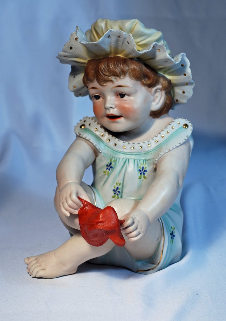 ADORABLE CONTA & BOEHME GERMAN BISQUE PIANO BABY: 50. LARGE CONTA & BOEHME GERMAN BISQUE PIANO BABY PLAYING WITH SOCK. 11”. Seated baby with deeply-sculpted face and brown hair, blue eyes, shaded brows, open/closed mouth with modeled detail between