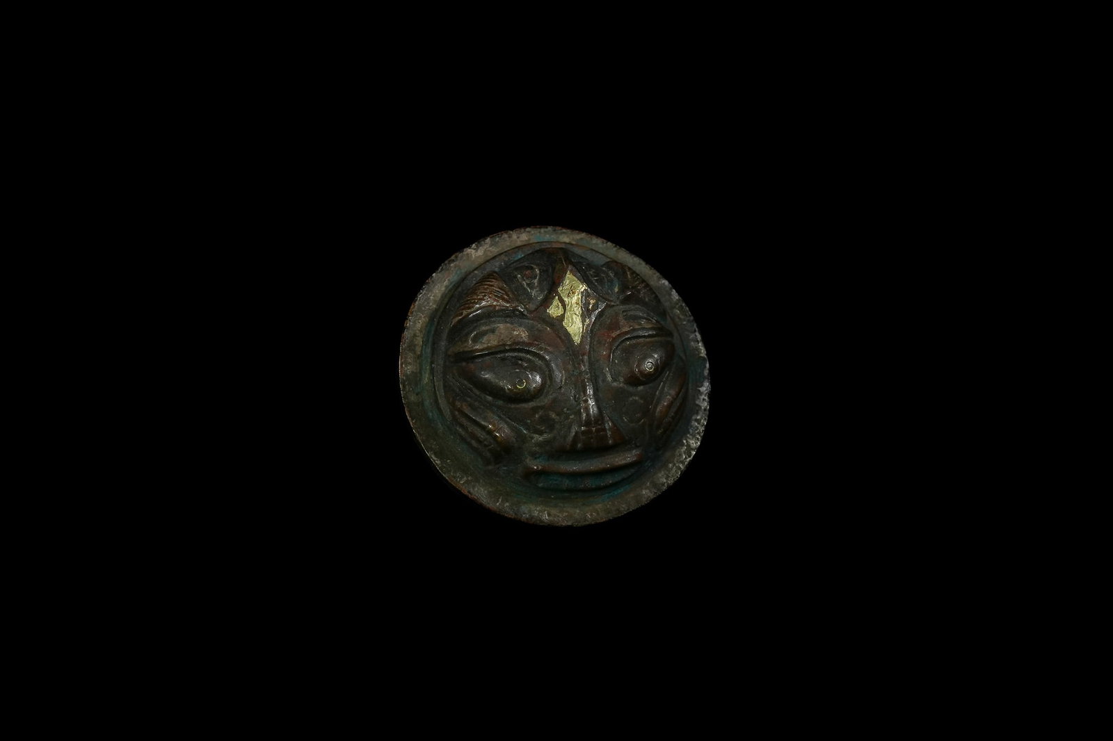 A Chinese Bronze Paperweight with Mask Motif, Han Dynasty.: A circular bronze paperweight featuring a boldly modelled mask-like face, defined by large rounded eyes, a broad nose, and a stylised mouth. L: Approximately 6cm