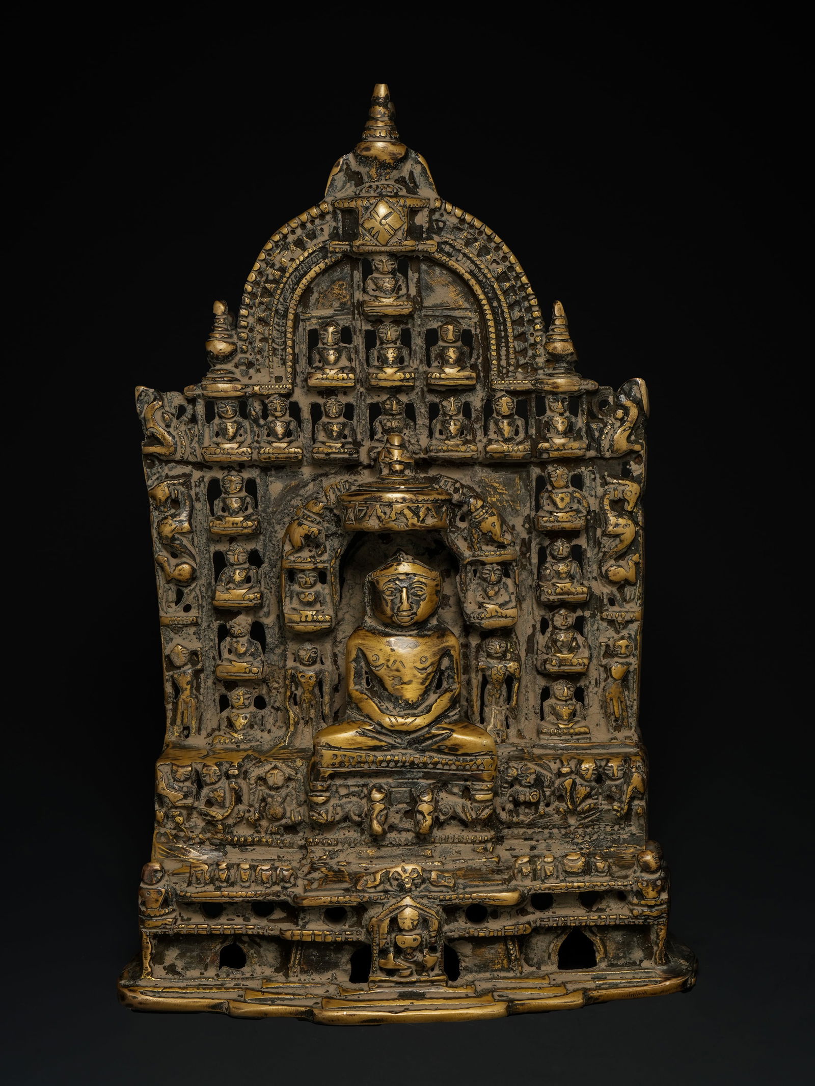An Indian Bronze Jain Chovisi Shrine, 19th Century or Later.: An Indian bronze Jain Chovisi shrine, cast in high relief and structured as a tiered architectural shrine. The composition centres on a seated Jina figure in dhyana posture within a recessed arched ni