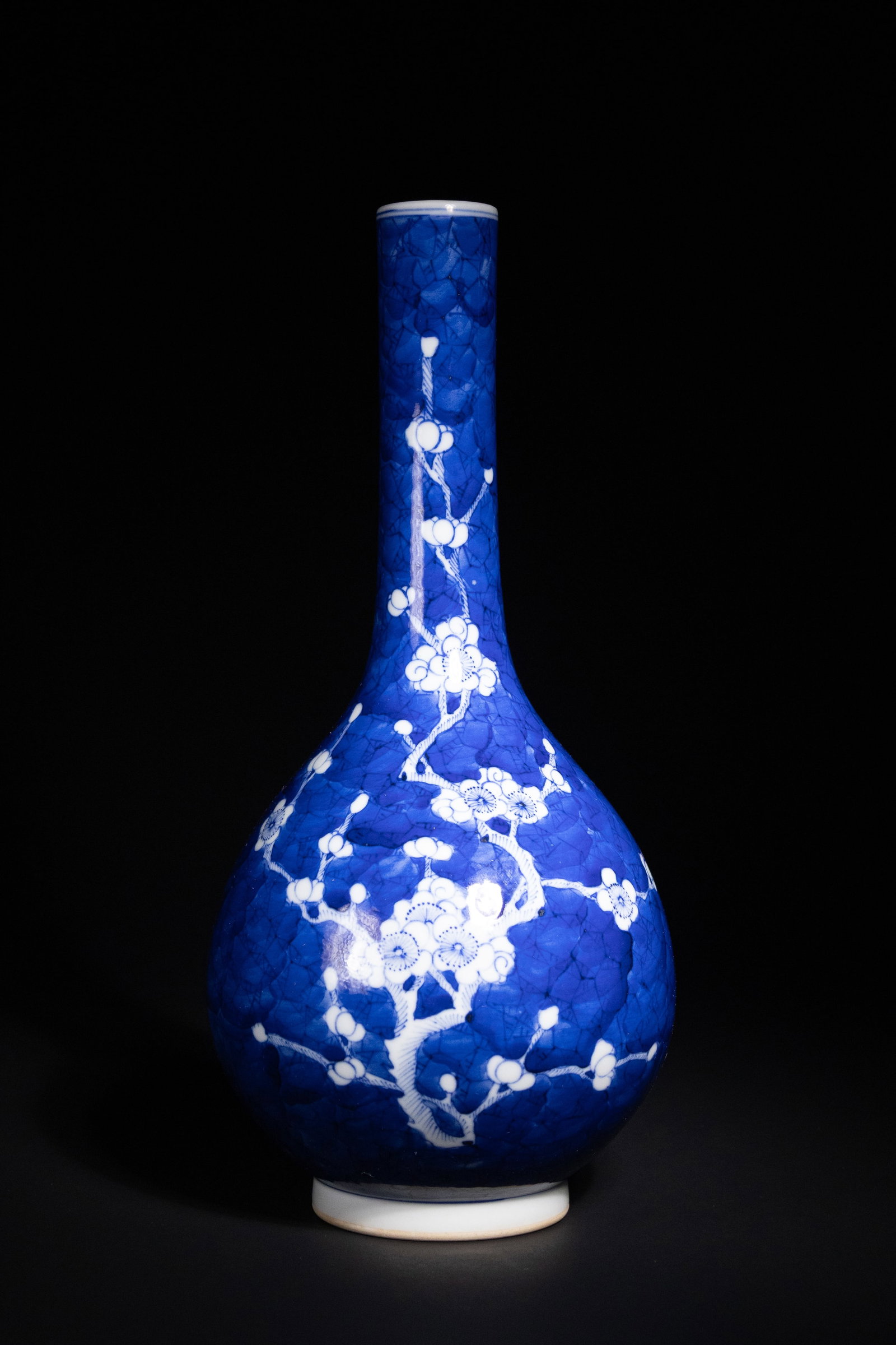A Chinese Blue and White Porcelain Ã¢â‚¬ï¿½Prunus BlossomÃ¢â‚¬â„¢ Vase: This porcelain vase is crafted in the bottle form with a tall, slender neck rising above a bulbous body. The rich cobalt blue ground is decorated with white prunus blossoms arranged in a continuous pa