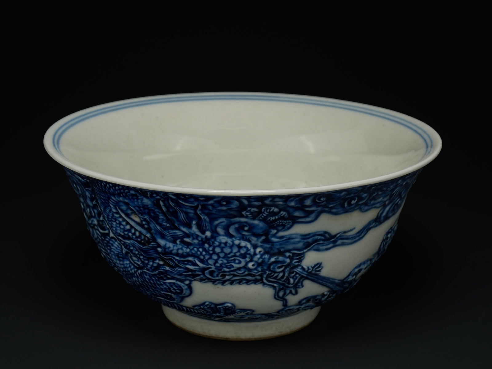 A Chinese Blue-and-White Dragon Bowl with Turbulent Waves.: The bowl is potted with deep, rounded sides rising to a gently everted rim, supported on a short, neatly finished foot. The exterior is densely decorated in underglaze cobalt blue with a continuous sc