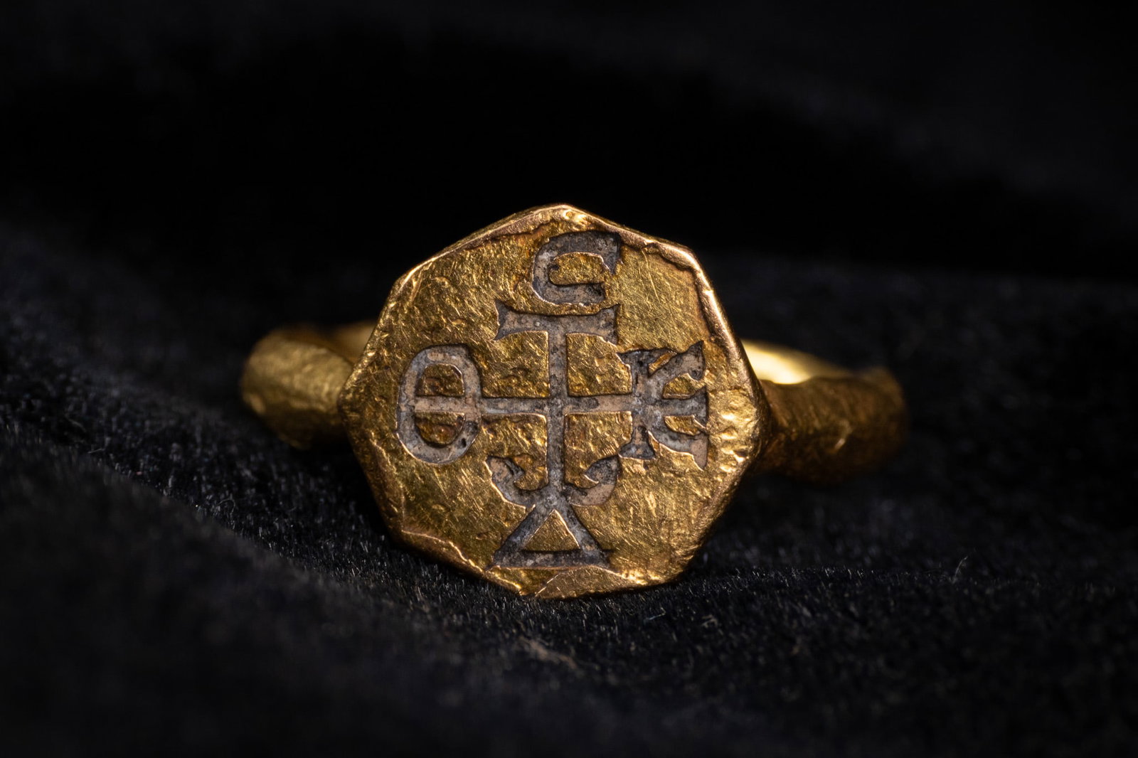 A BYZANTINE GOLD SIGNET RING WITH CRUCIFORM MONOGRAM, CIRCA 6TH-8TH CENTURY AD.: A hand-wrought high-carat yellow gold signet ring of the Byzantine period. The object features a flat, irregularly octagonal bezel joined to a faceted shank with an octagonal cross-section and a hamme
