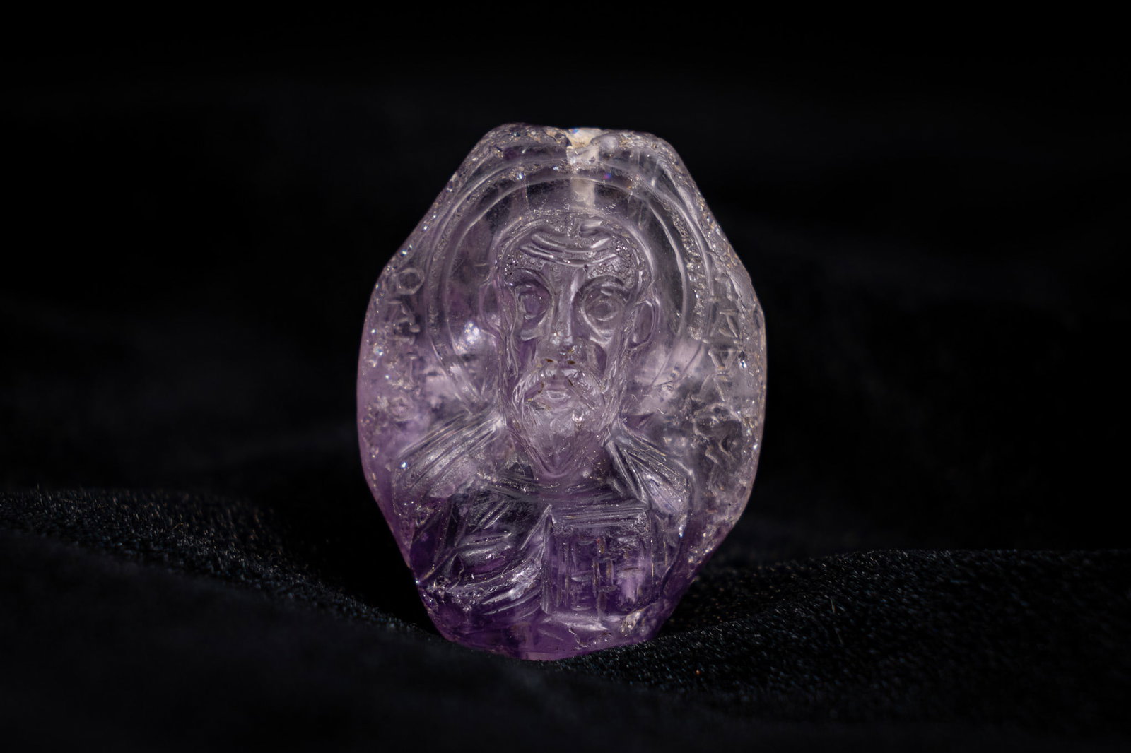 A BYZANTINE OR RUSSIAN DOUBLE-SIDED CARVED AMETHYST ICON PENDANT DEPICTING SAINT NICHOLAS AND SAINT: This double-sided icon pendant is carved from a single piece of translucent purple amethyst. One face features a relief carving of Saint Nicholas, depicted with a beard and halo while holding a Gospel
