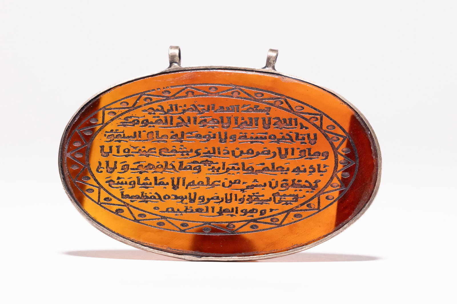 AN ISLAMIC OVAL SILVER-MOUNTED CARNELIAN AMULET PENDANT WITH CALLIGRAPHIC INSCRIPTION. (1 of 2)