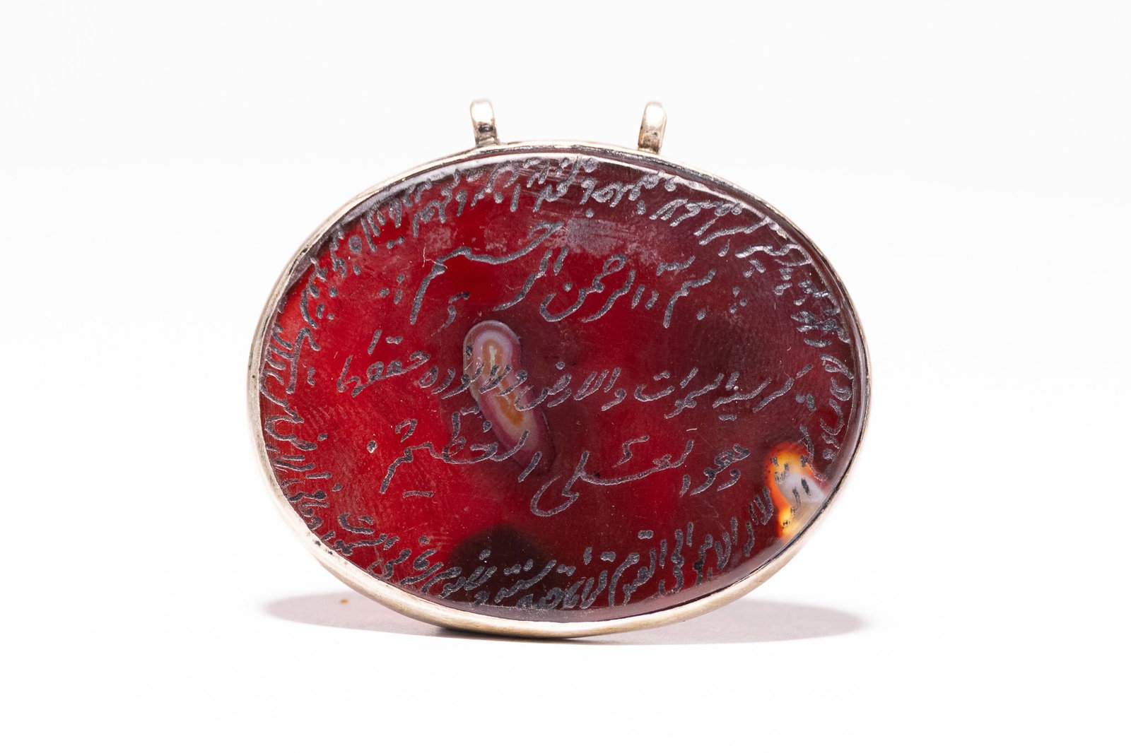 AN ISLAMIC ENGRAVED CARNELIAN AND SILVER TALISMANIC PENDANT WITH ARABIC INSCRIPTIONS.: This item is an oval, flat-backed carnelian pendant, often referred to as a hili or lawh, mounted in a simple silver frame. The primary stone is a deep red carnelian showing natural translucent and da