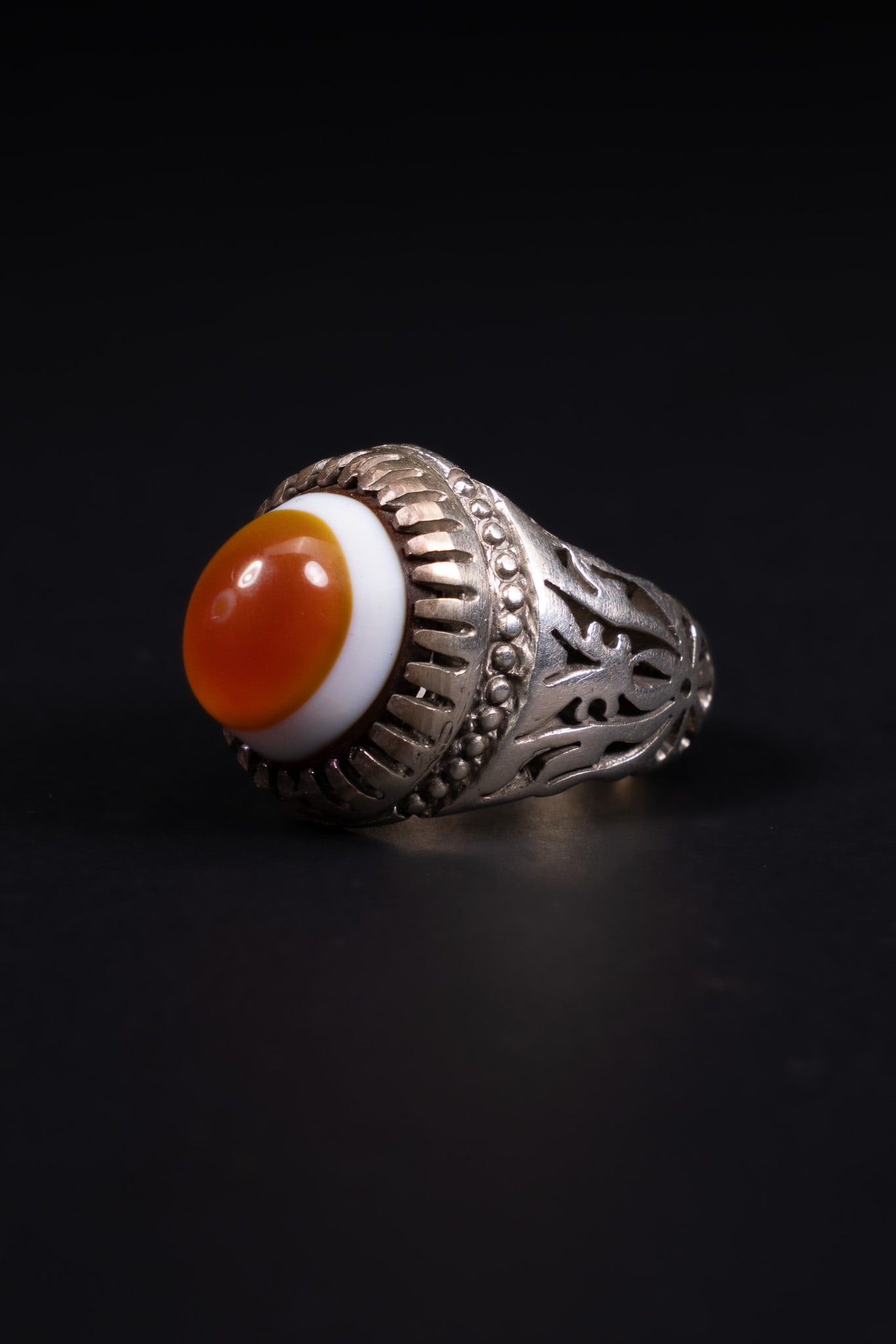 A YEMENI SILVER AND BANDED AGATE STATEMENT RING.: A Yemeni statement ring featuring a large oval cabochon banded agate, commonly referred to as Yemeni Aqeeq. The stone displays a translucent orange-brown centre surrounded by a distinct white outer ba