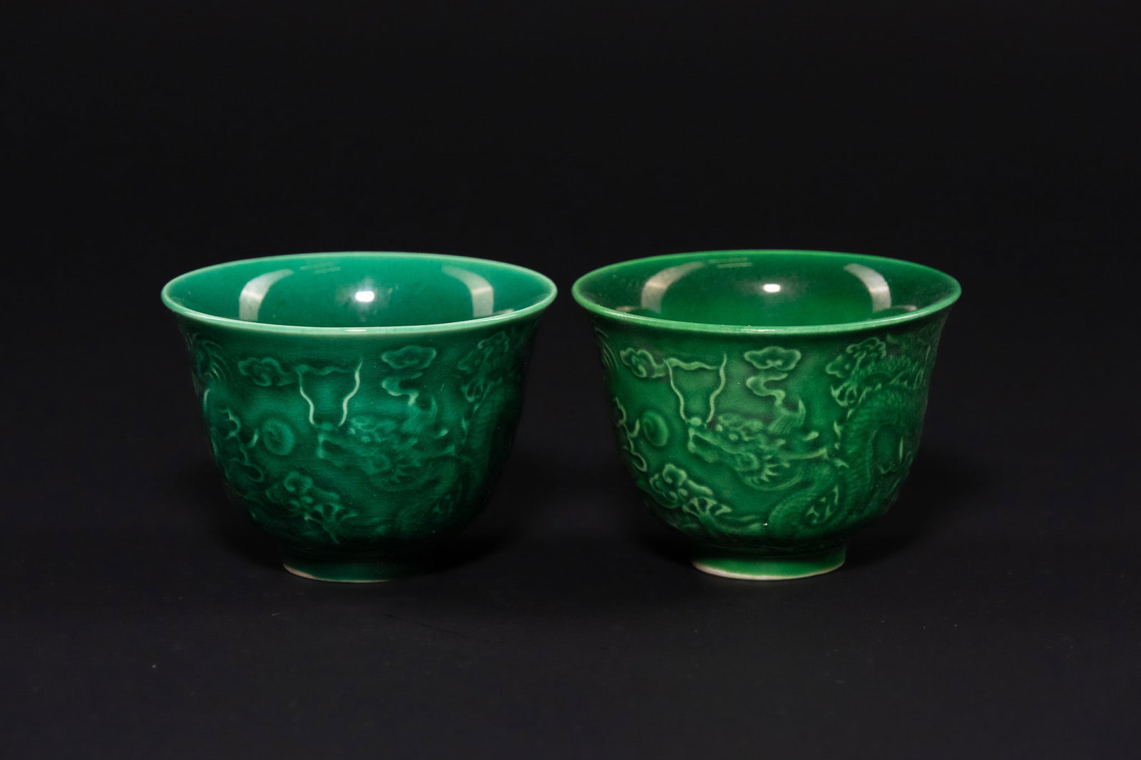 A CHINESE PAIR OF EMERALD GREEN-GLAZED PORCELAIN 'DRAGON' CUPS, LATE QING DYNASTY OR REPUBLIC: A pair of fine porcelain wine or tea cups, each expertly decorated to the exterior with a moulded and incised design featuring two five-clawed imperial dragons pursuing flaming pearls amidst a ground