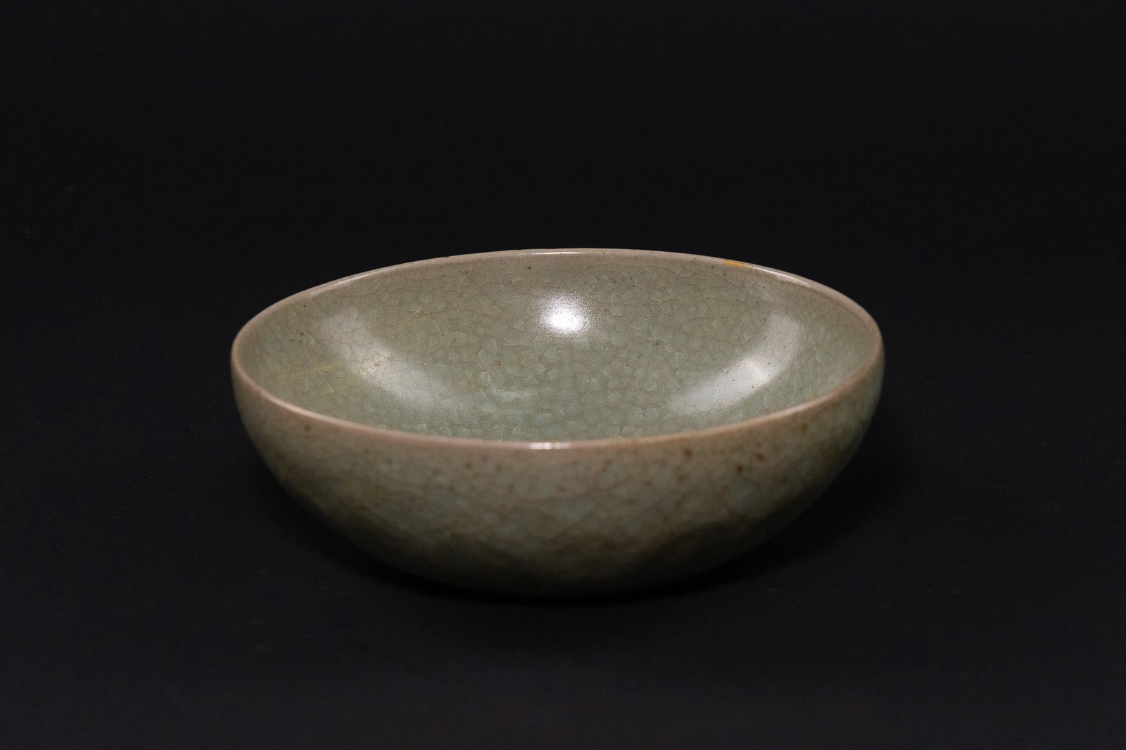 A CHINESE CELADON STONEWARE CRACKLE-GLAZED BOWL.: The stoneware body is potted with deep rounded sides and a slightly incurved rim, entirely covered in a thick, unctuous glaze of pale grey-green colour. The glaze is suffused with a dense and uniform