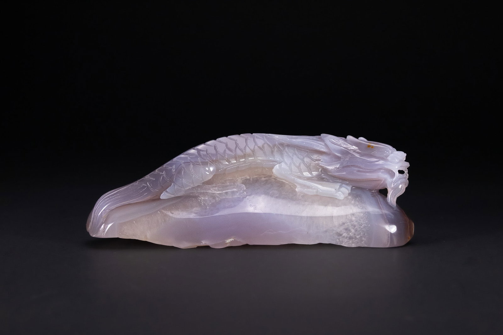 A CHINESE CARVED AGATE FIGURE OF A DRAGON.: A Chinese carved agate sculpture depicting a sinuous dragon reclining across the natural form of the stone. The dragon is rendered with a long, scaled body, arched back, and stylised head with open mo