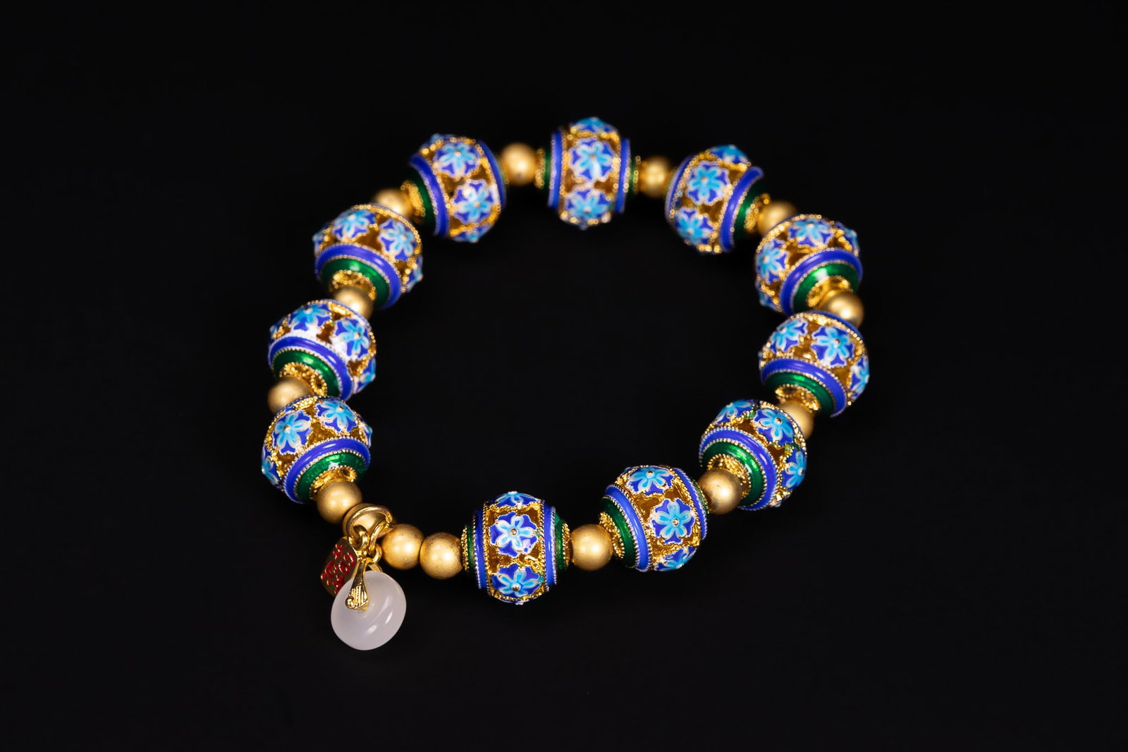 A CHINESE POLYCHROME ENAMEL AND WHITE JADE BEADED STRETCH BRACELET.: A beaded stretch bracelet featuring eleven barrel-shaped beads decorated with polychrome enamel. The enamel work is executed in shades of blue, green, and white, depicting stylised floral motifs withi