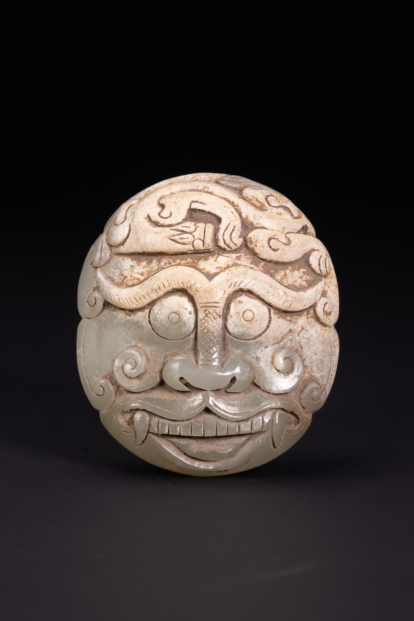 A CHINESE ARCHAISTIC PALE CELADON JADE MYTHICAL BEAST MASK FITTING. (1 of 2)