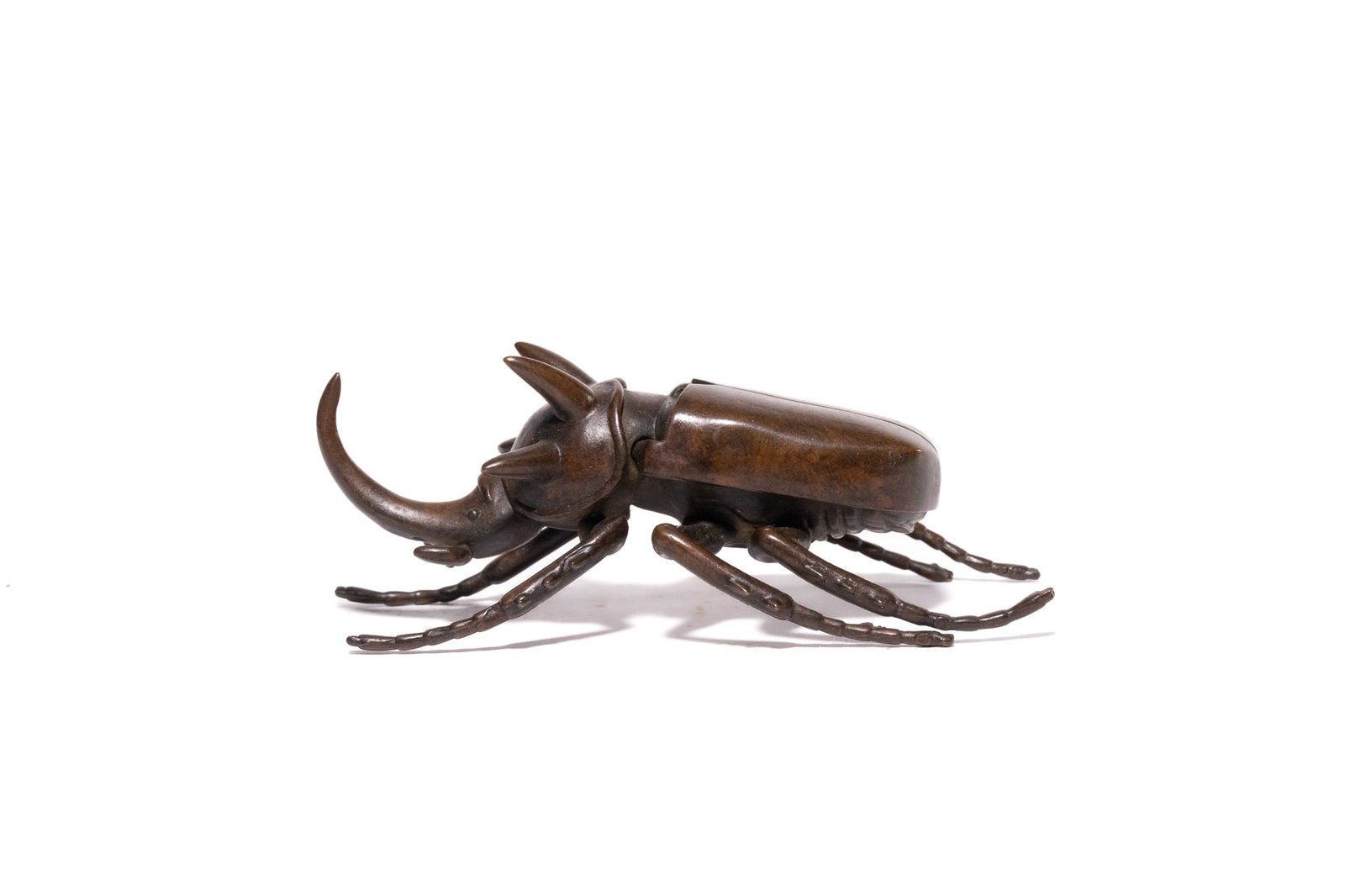 A JAPANESE BRONZE OKIMONO OF A RHINOCEROS BEETLE.: A naturalistically cast bronze model of a five-horned rhinoceros beetle, Eupatorus gracilicornis, attributed to the Japanese Meiji period. The beetle is rendered with anatomical precision, featuring a
