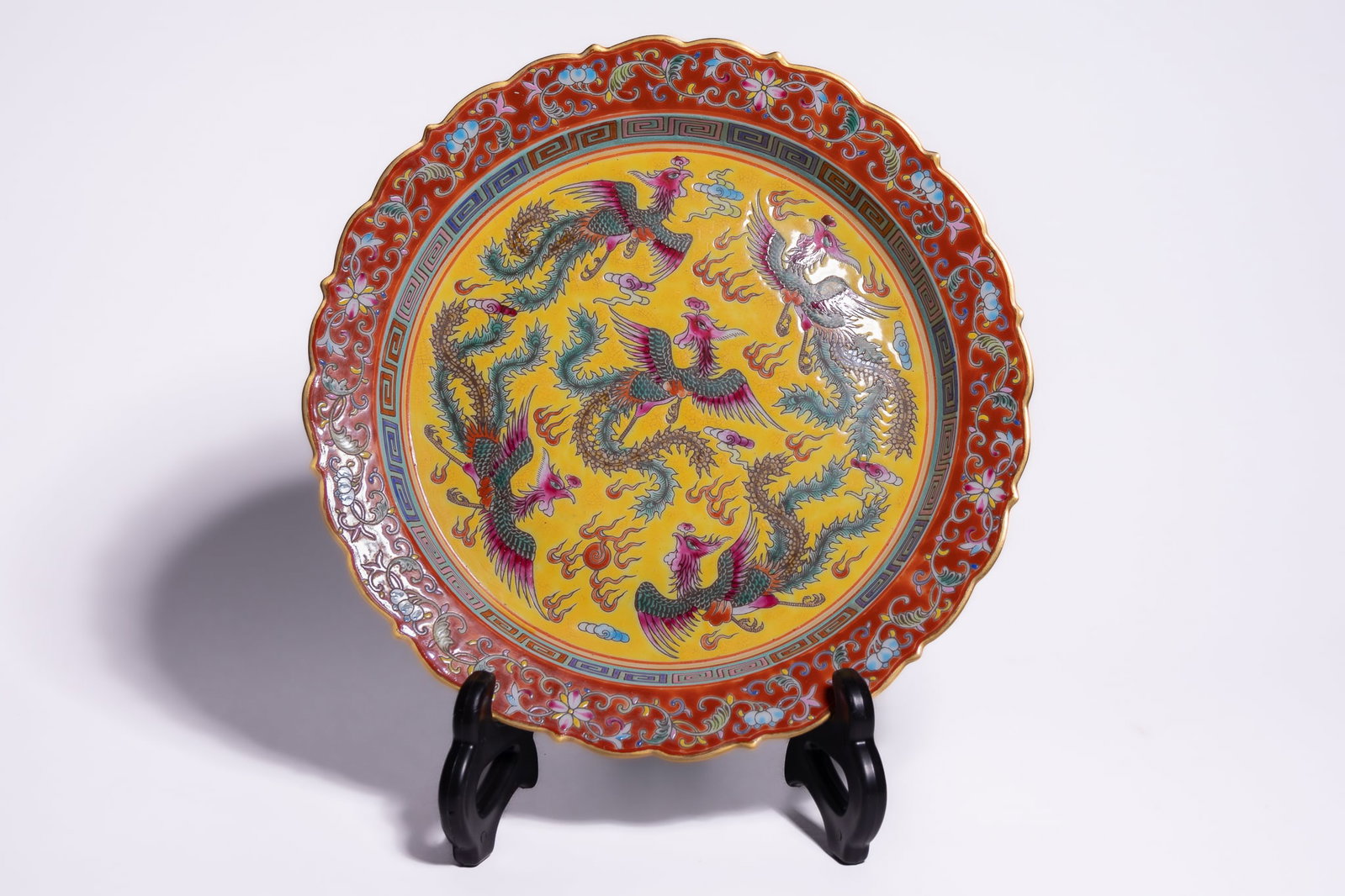 A CHINESE FAMILLE ROSE YELLOW GROUND PHOENIX DISH, YONGZHENG MARK.: This foliate-rimmed porcelain dish is decorated in the famille rose (fencai) palette. The interior centre features five phoenixes (fenghuang) in flight amidst stylised clouds and fire motifs, set agai