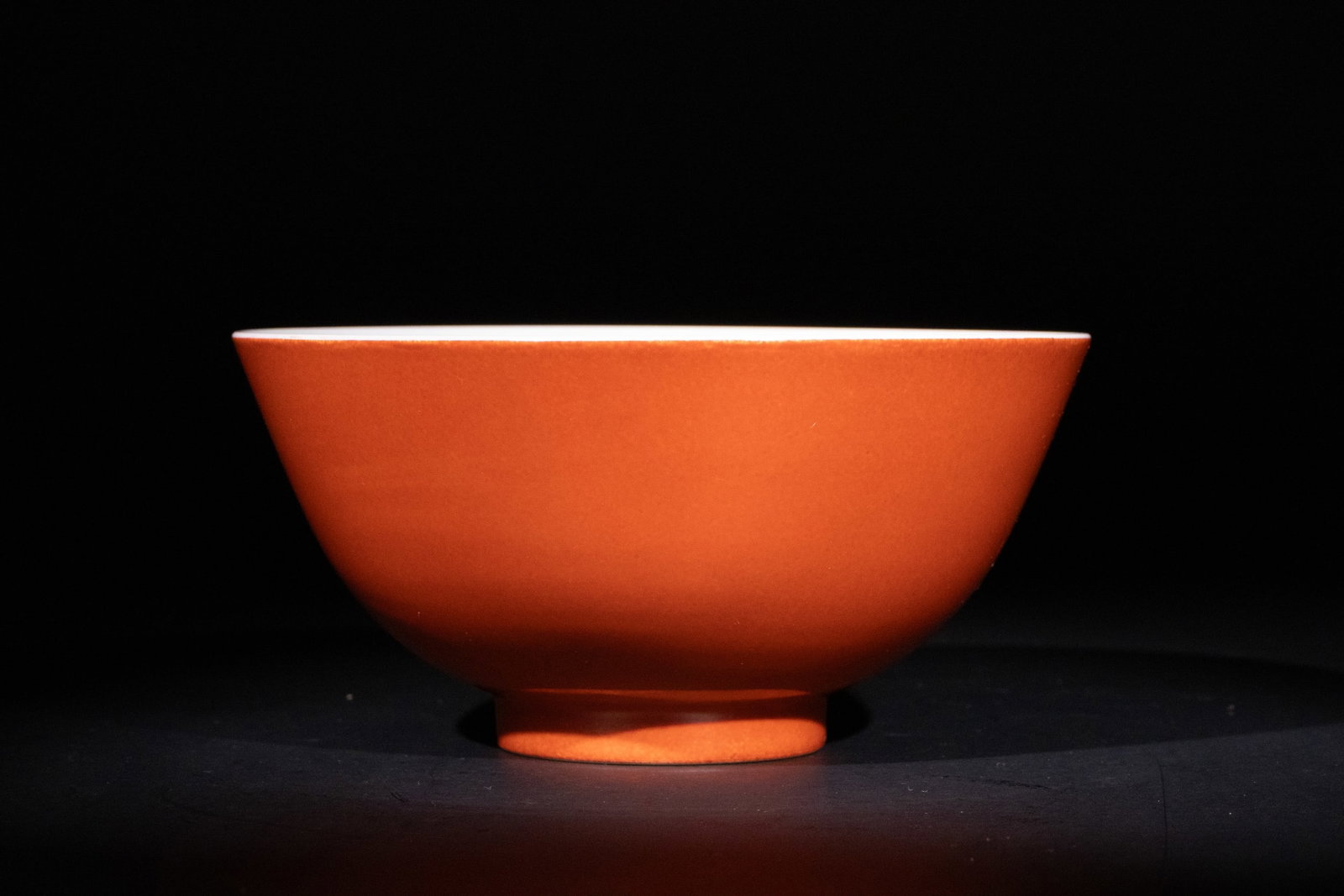 A Chinese Coral-Red Porcelain Bowl with Six Character Marks to the Base: A Chinese porcelain bowl with a smooth coral-red exterior glaze, contrasting with its white interior. The bowl has a gently flaring rim and a slightly recessed foot. The base bears a six-character mar