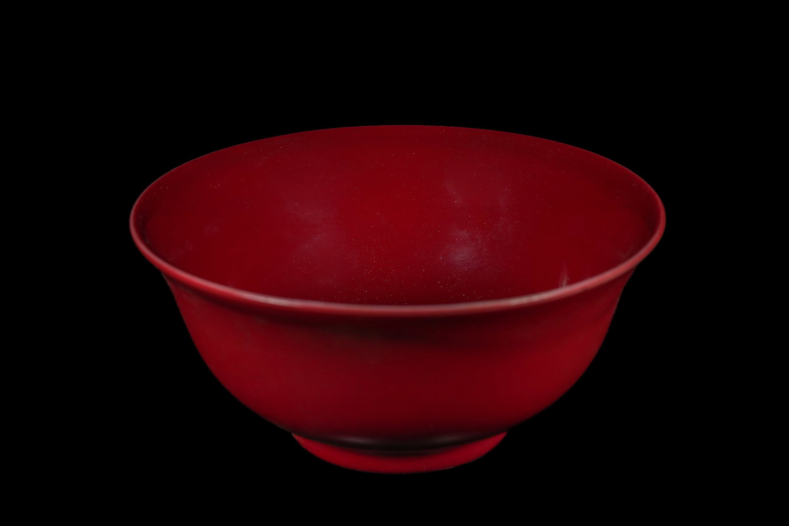 A Chinese Monochrome Red-Glazed Porcelain Bowl, Yongzheng Mark: A deep, round ceramic porcelain bowl characterized by its uniform, vibrant monochrome red glaze with a glossy finish covering both the interior and exterior. The bowl features a slightly everted rim a