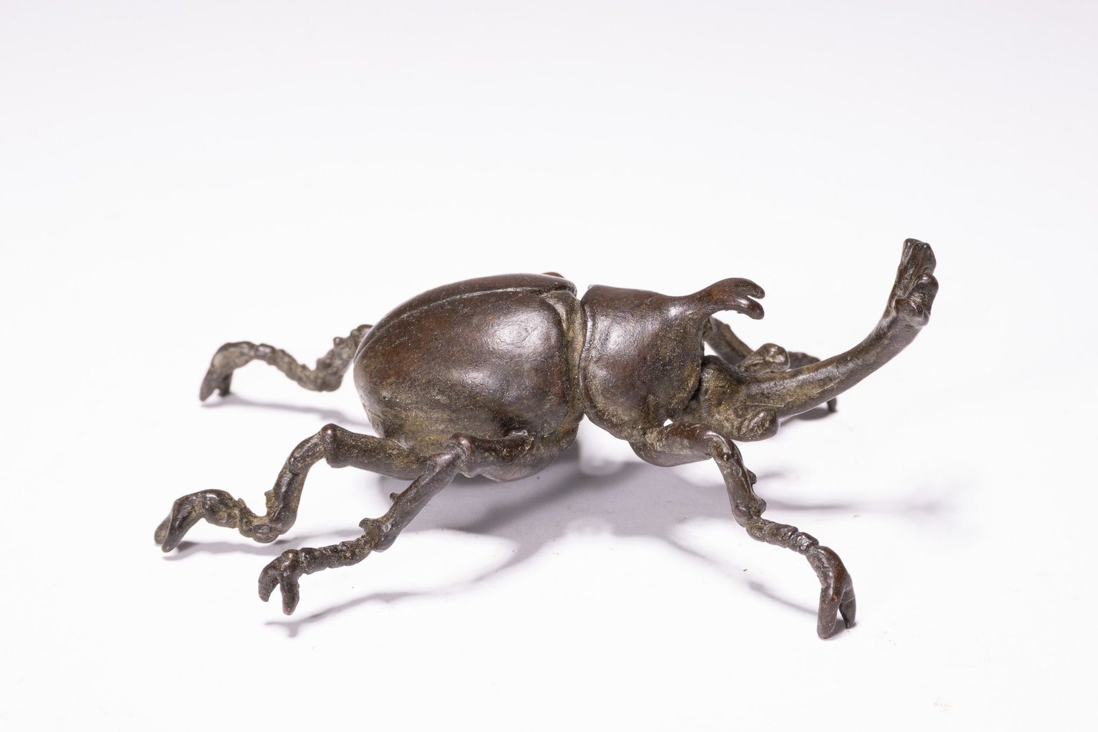 A JAPANESE MEIJI PERIOD BRONZE RHINOCEROS BEETLE OKIMONO.: A Japanese bronze sculpture (okimono) depicting a rhinoceros beetle (Allomyrina dichotoma), commonly known as kabutomushi. The piece is cast with realistic anatomical features, including the character