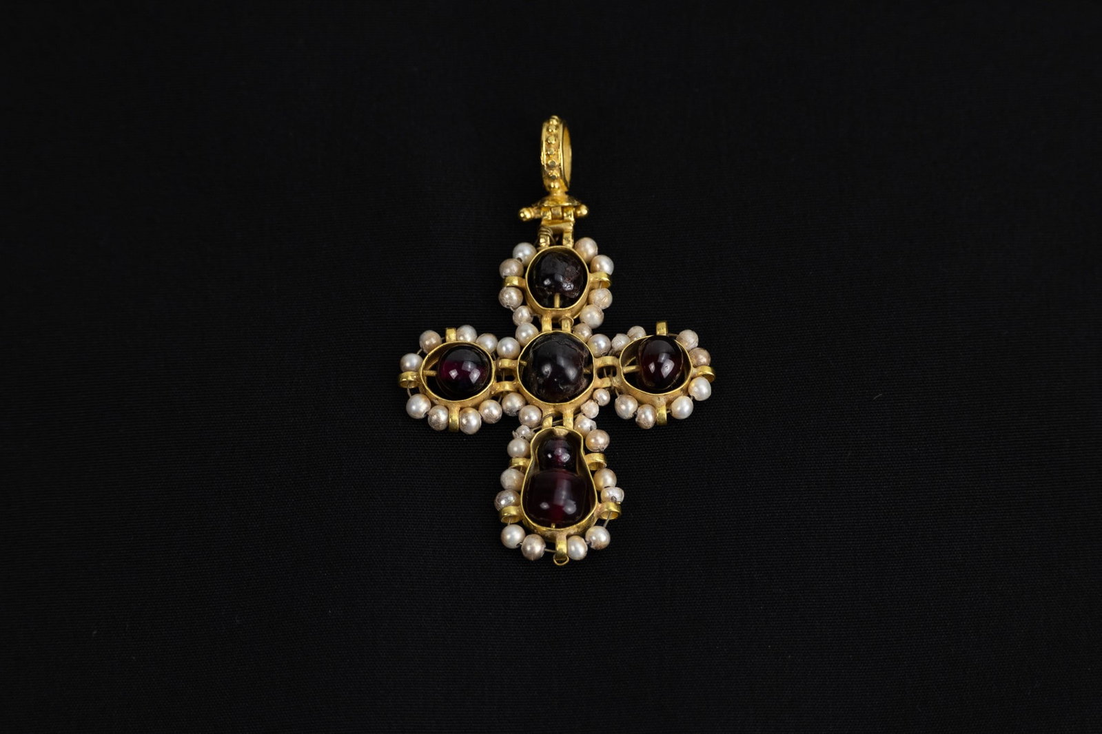 AN EASTERN EUROPEAN BYZANTINE GOLD CROSS PENDANT DECORATED WITH GARNETS AND PEARLS, 18TH CENTURY.: The cross features a central garnet cabochon, surrounded by four additional garnet stones at each point of the cross, symbolizing richness and spiritual significance. The garnets are encircled by lust
