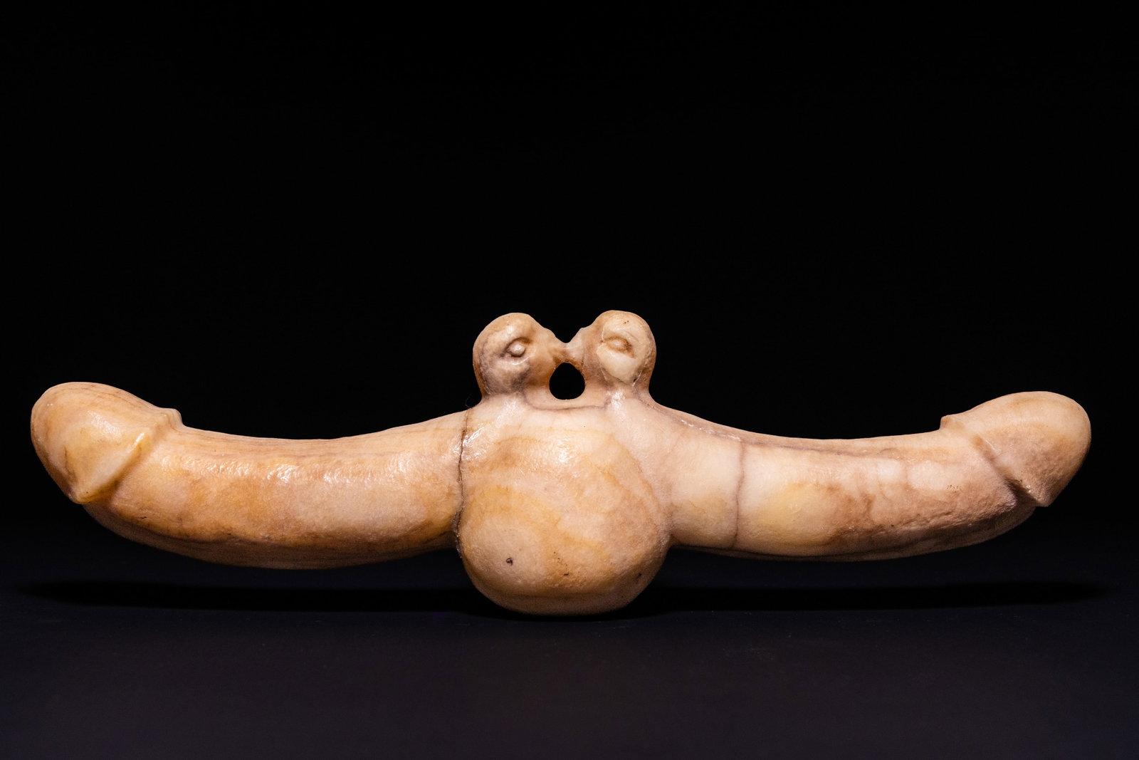 A GREEK MARBLE DOUBLE-ENDED PHALLIC AMULET, POSSIBLY CIRCA 3RD CENTURY AD.: A carved marble double-ended phallic amulet or votive object, formed with two opposing phalli extending horizontally from a prominent rounded central element. Above the centre are two stylised rounded