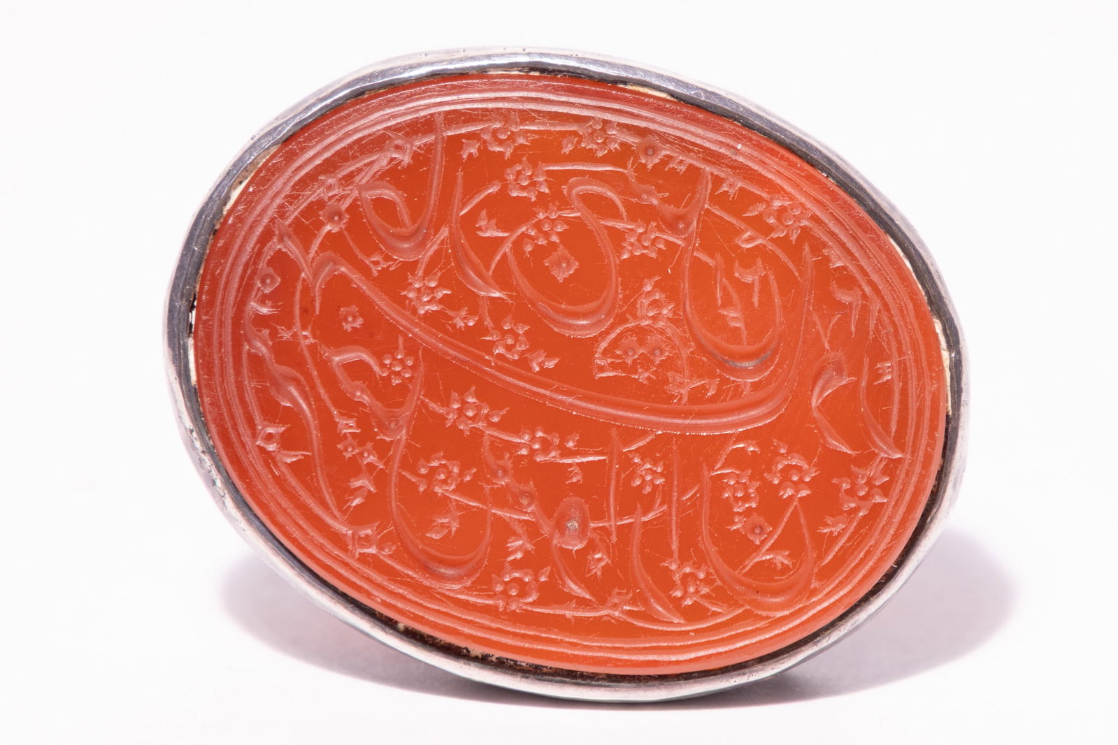 A PERSIAN SILVER AND CARNELIAN INTAGLIO DESK SEAL.: A Persian desk seal comprising an oval carnelian intaglio set in a silver mount. The orange-red carnelian is finely engraved with Persian calligraphy in Nasta'liq script, interspersed with small flora