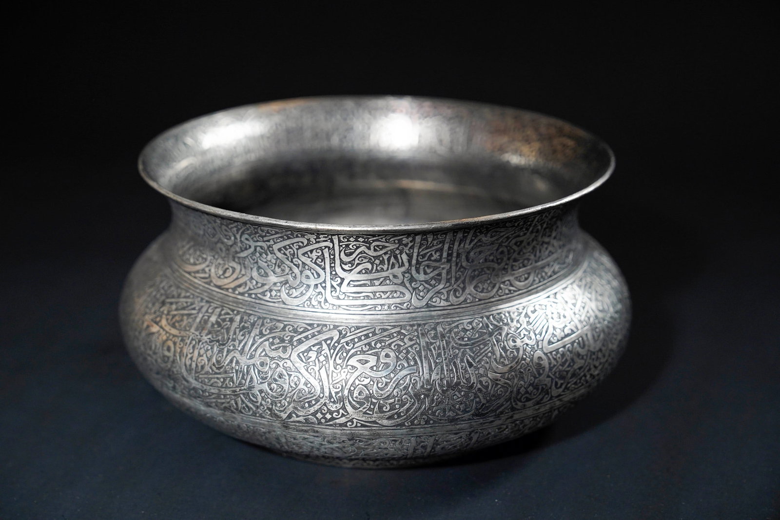 AN INDIAN DECCAN ENGRAVED COPPER KASHKUL BEGGAR'S BOWL, 17THâ€“18TH CENTURY.: An Deccan Indian copper beggarâ€™s bowl engraved in high detail with continuous bands of elegant Islamic calligraphy in thuluth script. The inscriptions wrap around the entirety of the bulbous