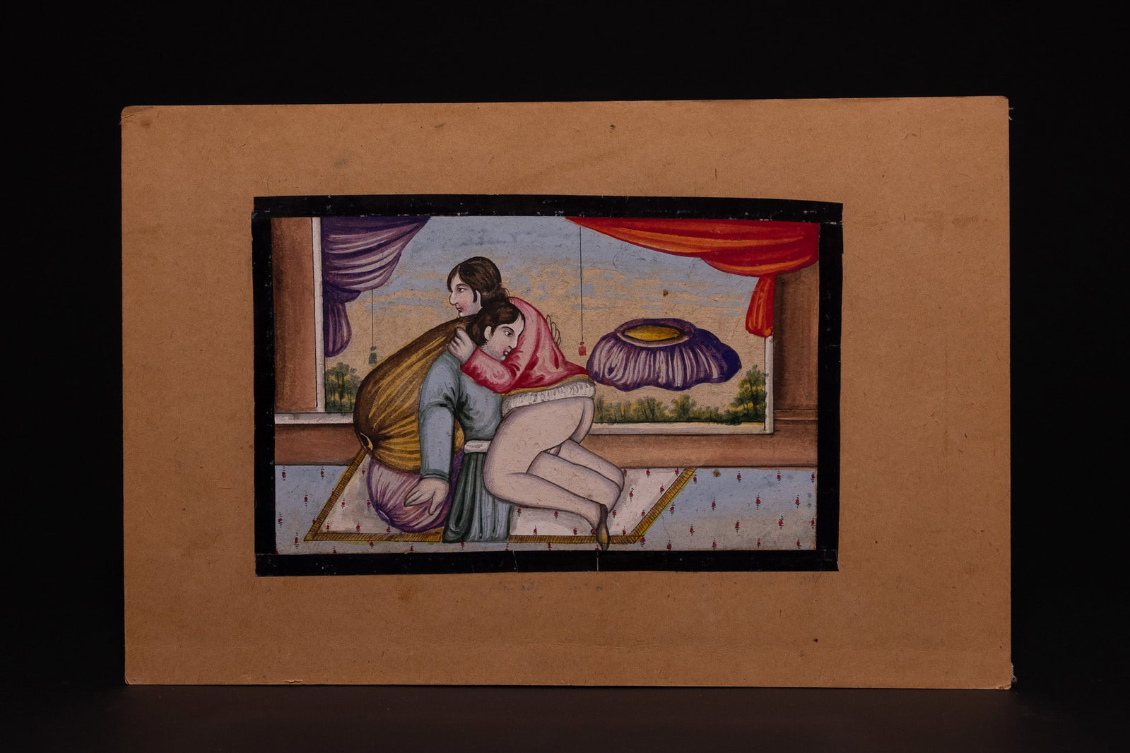 A QAJAR EROTIC MINIATURE PAINTING, 19TH CENTURY.: The work is rendered in gouache and tempera on paper, mounted onto a tan-coloured card. The composition depicts an amorous scene between two figures in profile. A man, seated on a patterned rug and le