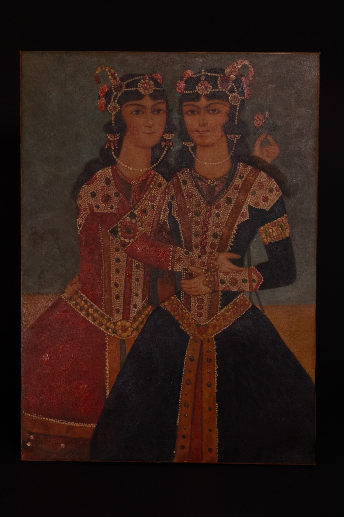 A QAJAR STYLE PORTRAIT OF TWO SISTERS OIL ON CANVAS, POSSIBLY 19TH CENTURY.: An oil painting on canvas depicting two female figures, traditionally identified as twins or sisters, executed in the Qajar style. The figures are shown from the waist up against a dark mottled backgr